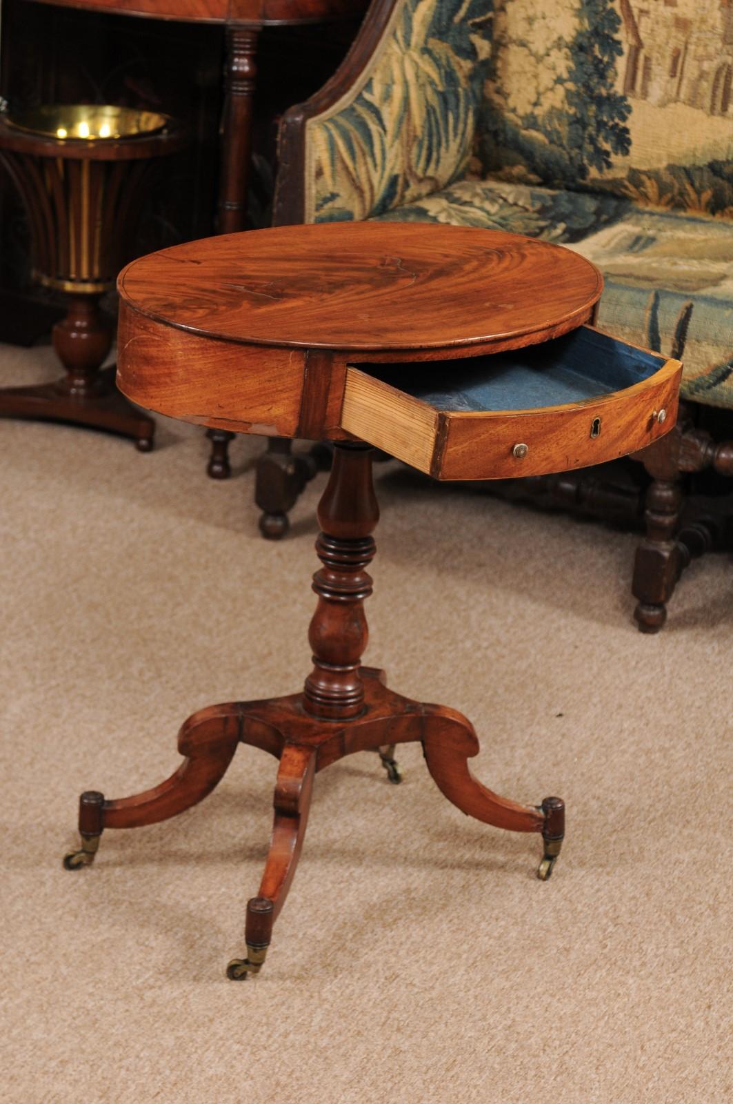 The Regency English mahogany side table with oval form top with drawer and turned pedestal below terminating in four splayed legs resting on brass castors. 

 