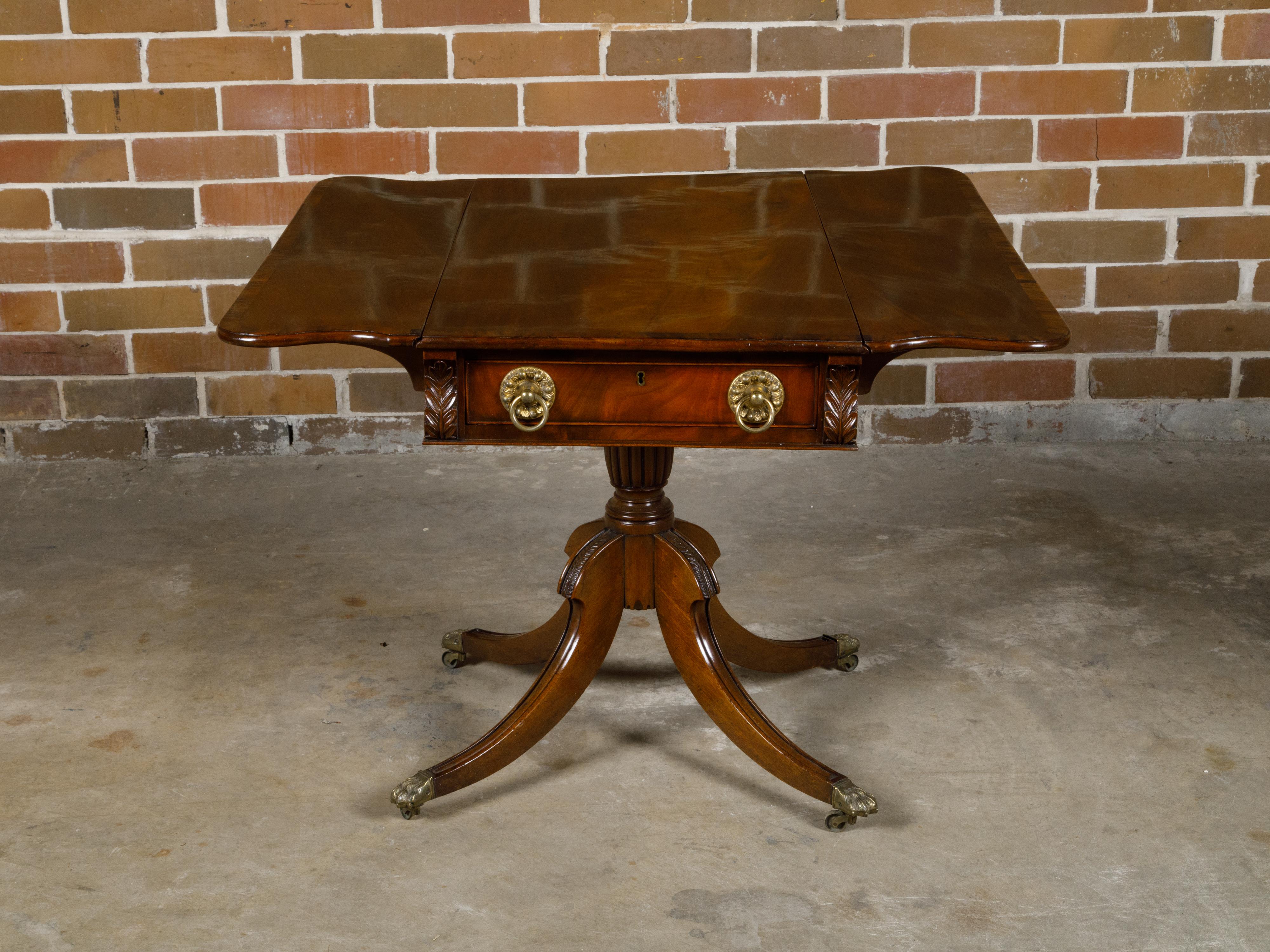 An English Regency period mahogany Pembroke table from the 19th century with drop leaves, cross-banding, single drawer and quadripod base. This exquisite English Regency period mahogany Pembroke table from the 19th century marries functionality with