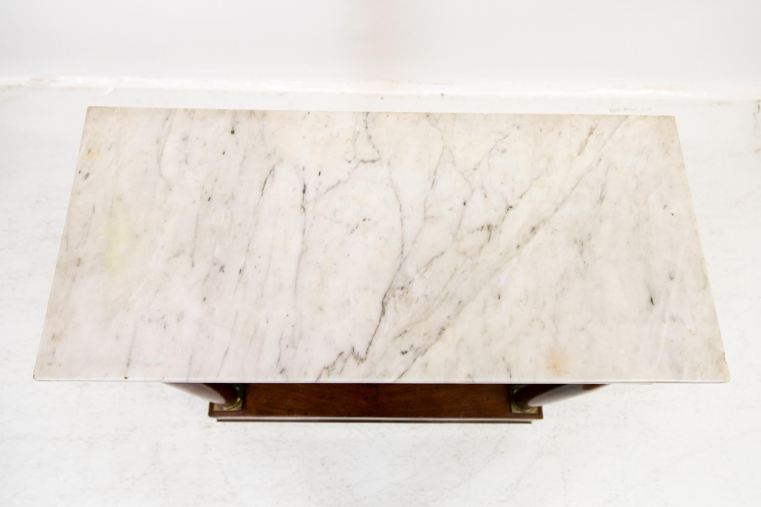 This console table has a cove molding beneath the marble top. The apron is supported by free standing turned columns that have decorative brass capitals and bases. There is a mirror in the back that is framed with simulated pilasters that extend