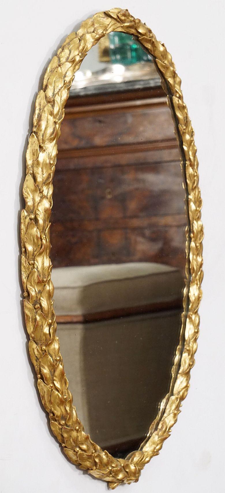 A fine English oval hall or wall mirror from the Regency Era, circa 1810, featuring a beautiful carved giltwood frame with a Neo-Classical foliate wreath design of laurel leaves.