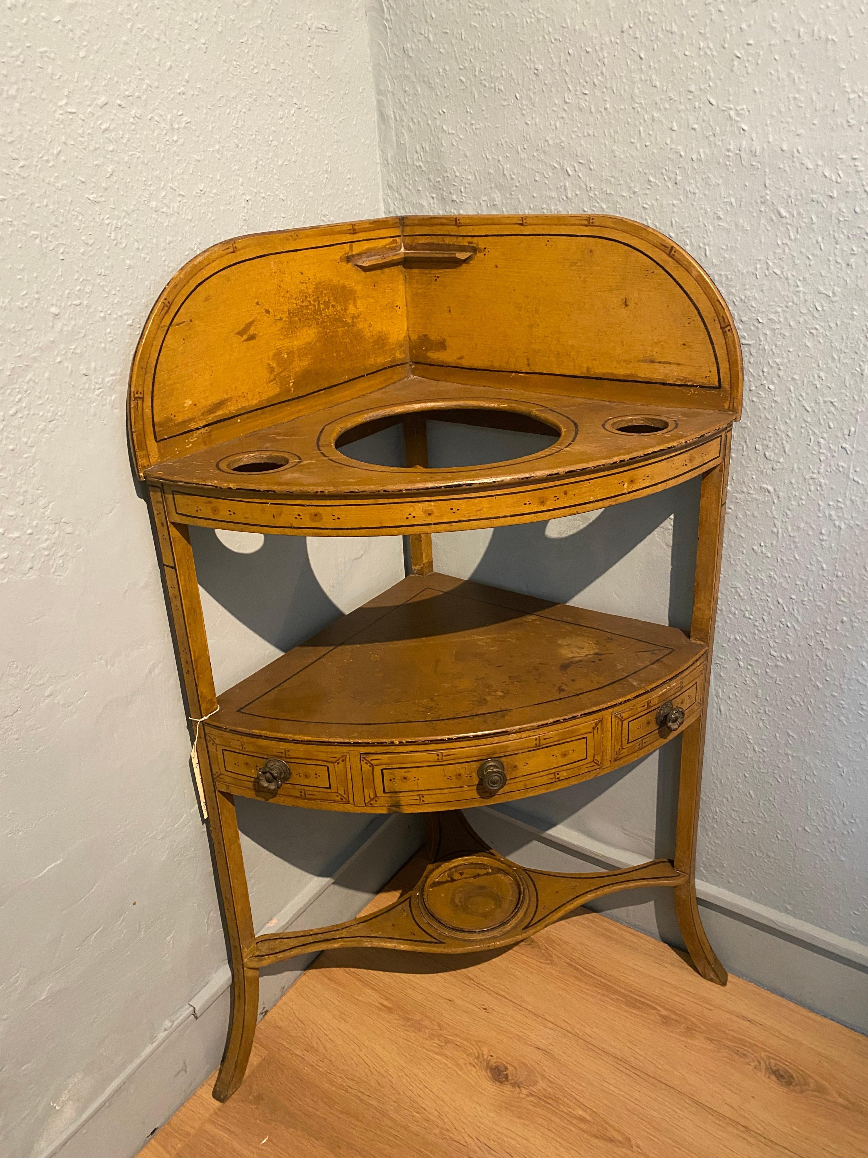 This attractive Regency simulated bamboo corner washstand, has its original paint. 
The upper section consists of a curved splash back and holding holes for a washbasin, shaving and toothbrush mugs. 
There is a single frieze drawer to the centre