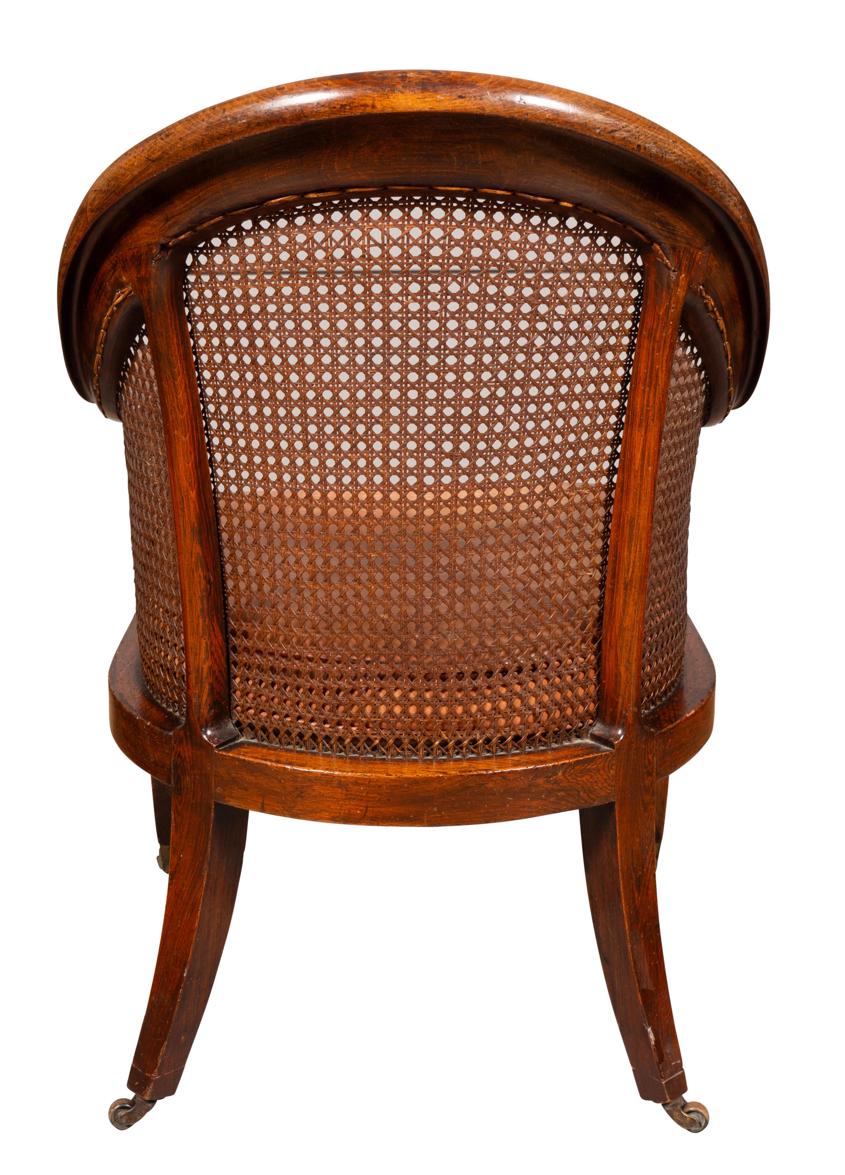 With arched back barrel form with caned back and sides, loose leather cushion and caned seat. Saber legs and casters.