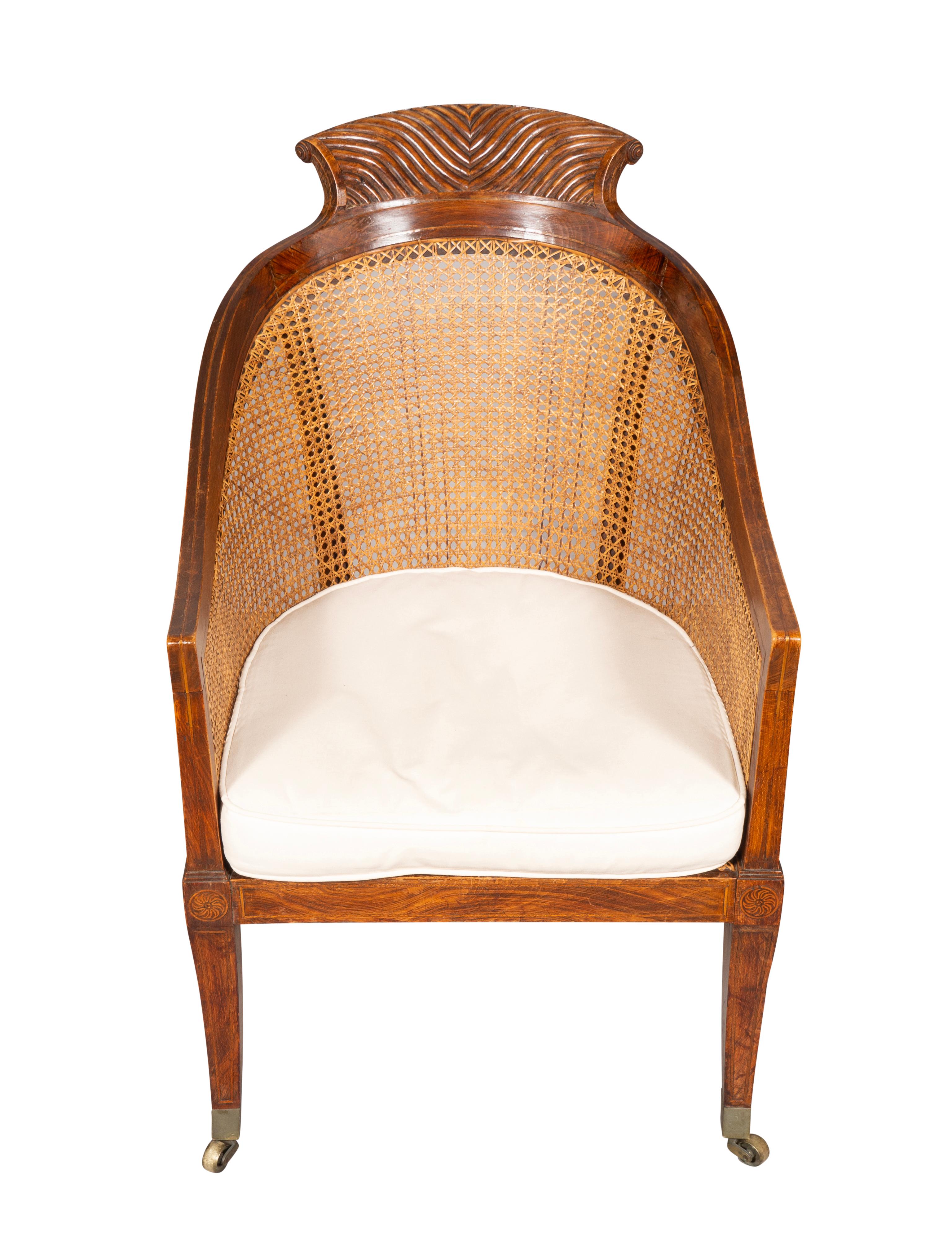 Wit arched crest rail with reeded scrolled carving over a caned back and seat. Down swept arms and saber legs ending on casters. Loose cushion seat.