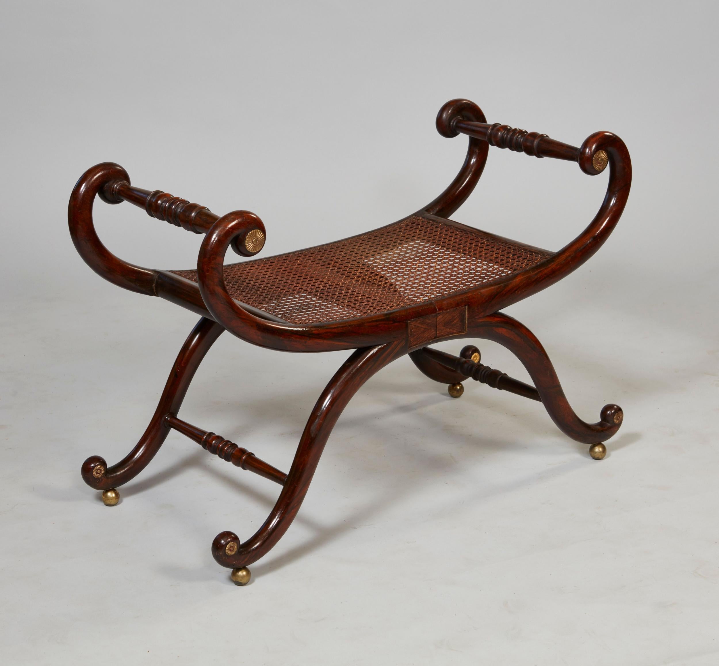 Fine English early 19th century faux rosewood and zebrawood grain painted bench with gilt brass rosettes and brass string inlay, the curled ends joined by turned stretchers over cane seat and standing on gracefully curved legs ending in scroll feet,