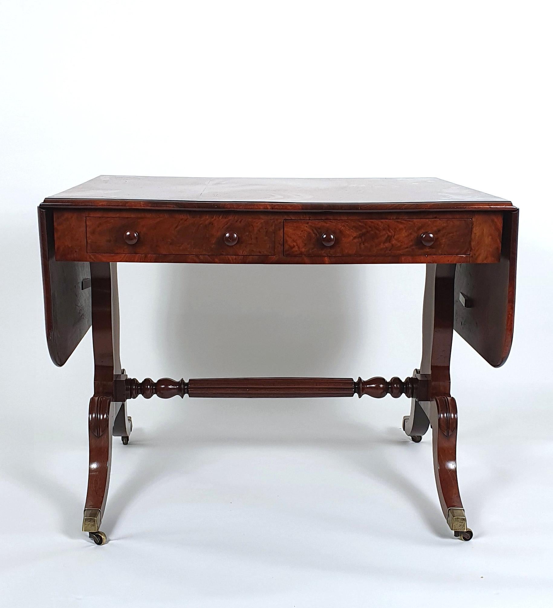 This very handsome and well-proportioned Regency figured solid mahogany sofa table features one true and one dummy drawer to each side and is supported on swept supports which are united by a central turned stretcher base. The table measures: 30 in,