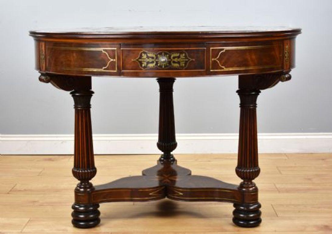 Il s'agit d'une table à tambour en acajou flammé incrustée de laiton de belle qualité, de style Régence, à la manière de John McLean. Le plateau segmenté, plaqué d'acajou et incrusté de laiton, entoure une étoile centrale. La frise lambrissée