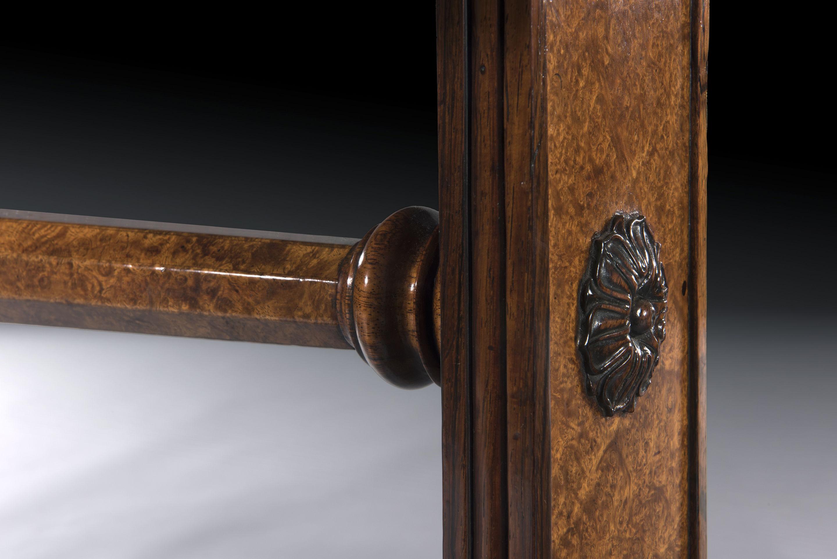 The rounded rectangular amboyna veneered top is crossbanded in rosewood with a shallow frieze veneered in amboyna and an applied solid rosewood moulding above a veneered facetted stretcher with a rosewood reeded ring-turned centrepiece. The elegant