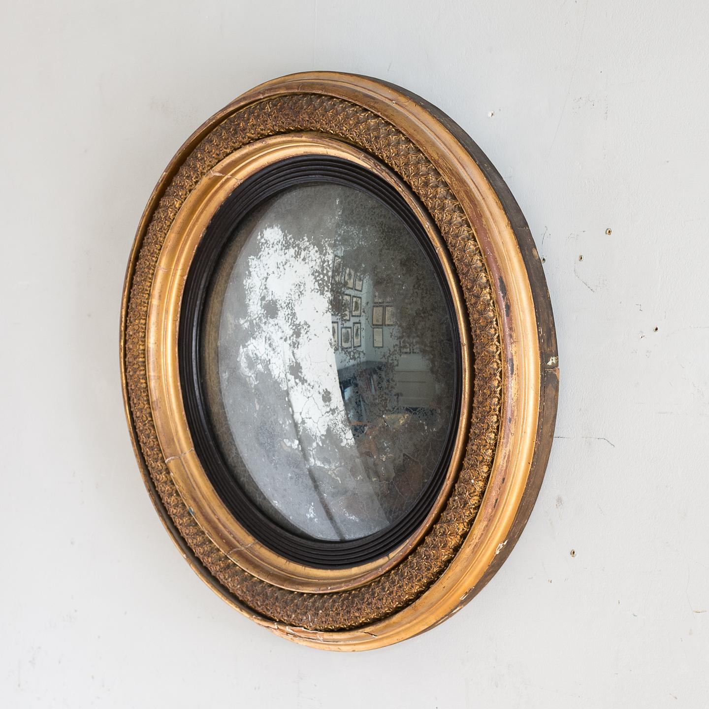 Regency gilded convex mirror, the unusual moulded composition frame with reeded ebonised slip surrounding original plate.