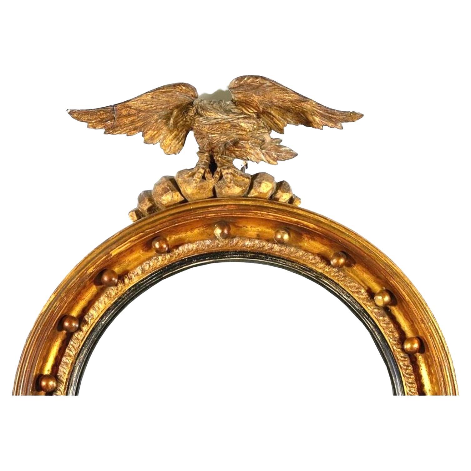 19th Century Regency or Federal Carved Giltwood Convex Bullseye Mirror with Eagle Pediment. Mirror is carved in giltwood and crowned with a boldly rendered eagle pediment. The circular frame is detailed with a series of raised gilt beads, a