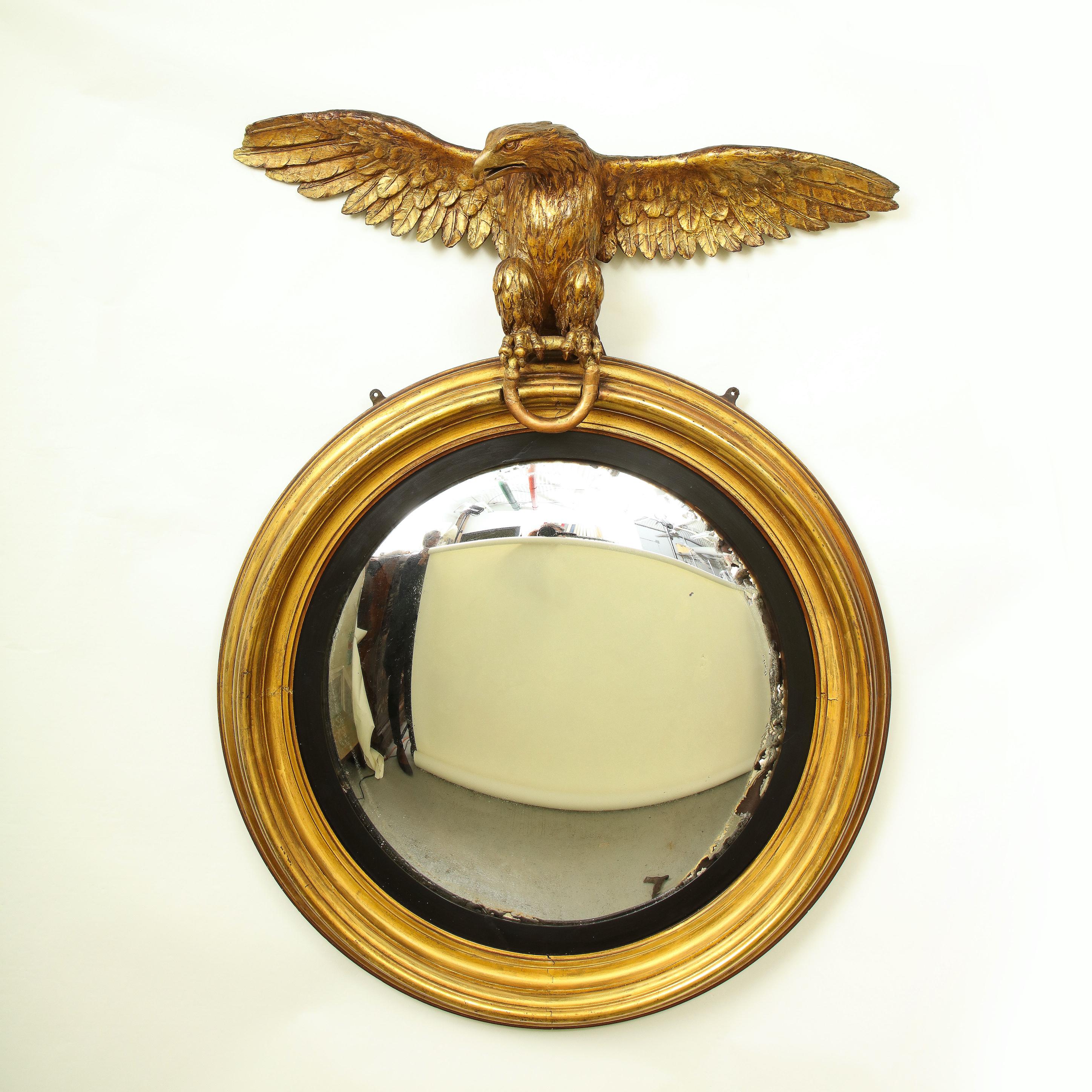 The circular convex mirror plate within a black slip and molded giltwood surround, surmounted by an outstretched eagle perched on ring.

Provenance: From the Collection of Mario Buatta, New York, NY.