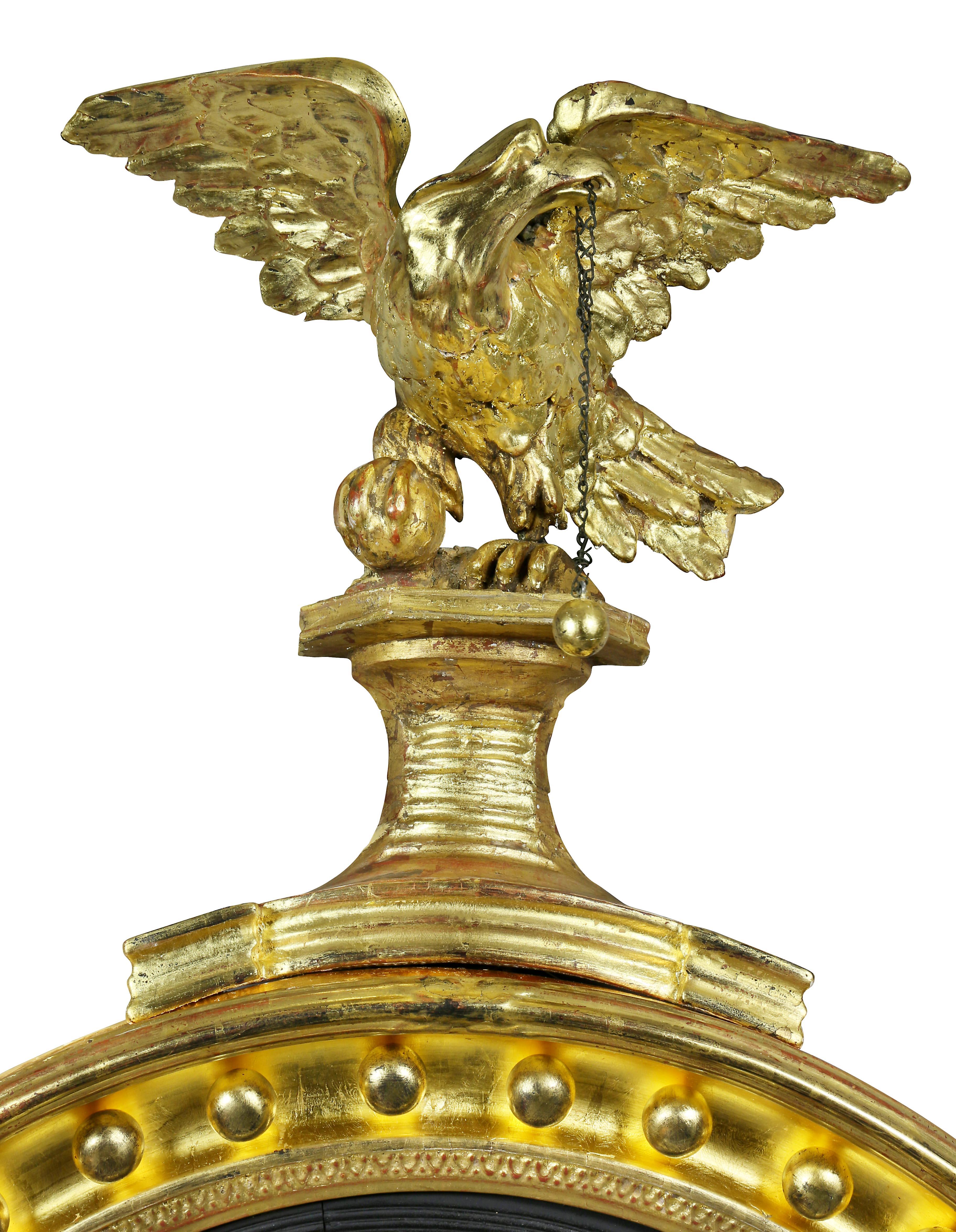 The eagle standing with wings spread on a plinth over a convex mirror plate set in a conforming cove molded frame with mounted spherules, the base of mirror frame with mounted acanthus carved decoration.