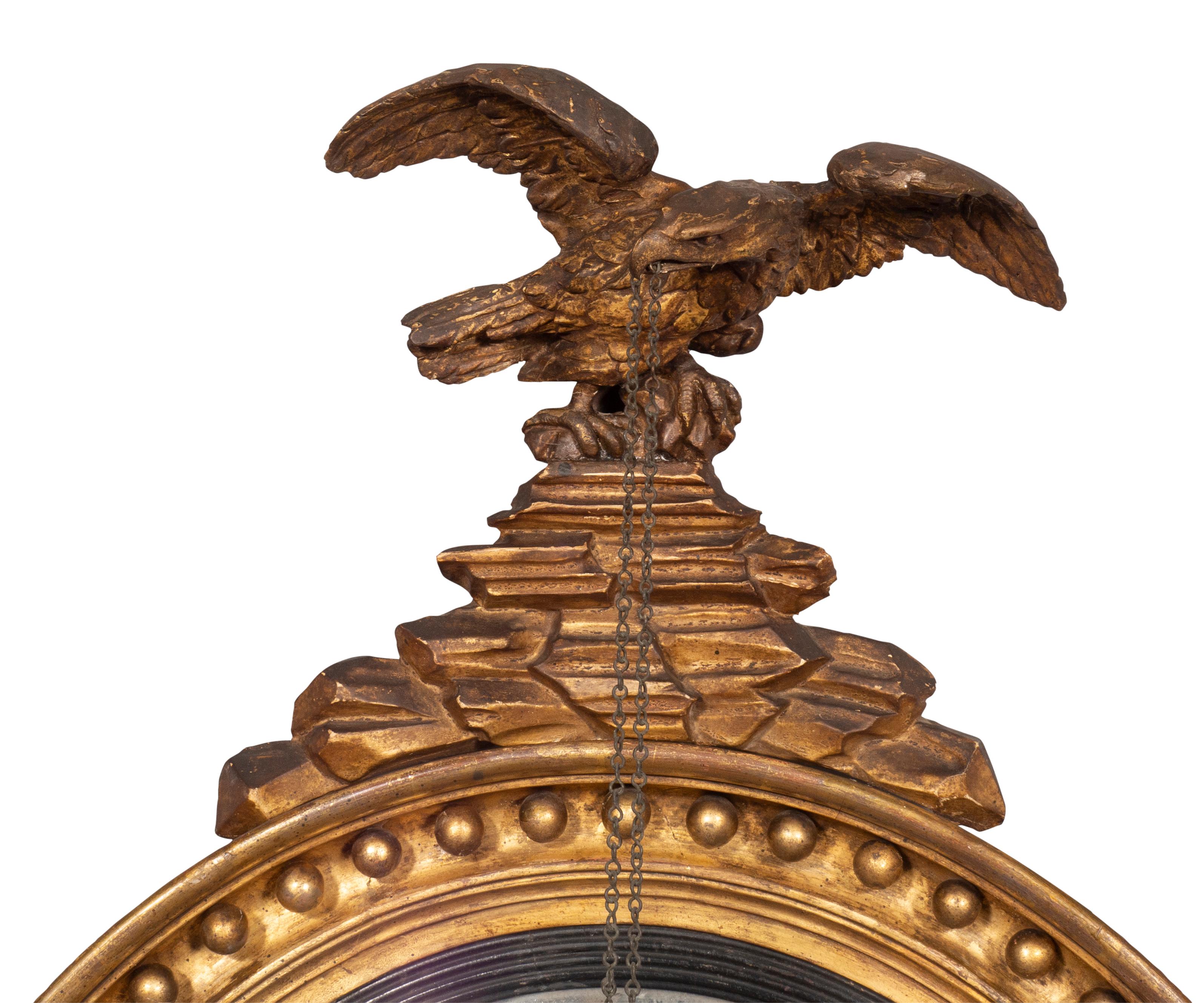 With eagle crest. The eagle holding a chain in its beak suspending two spheres. Circular mirror frame with spherules and central convex glass. Original glass with oxidation. Original gilded surface.