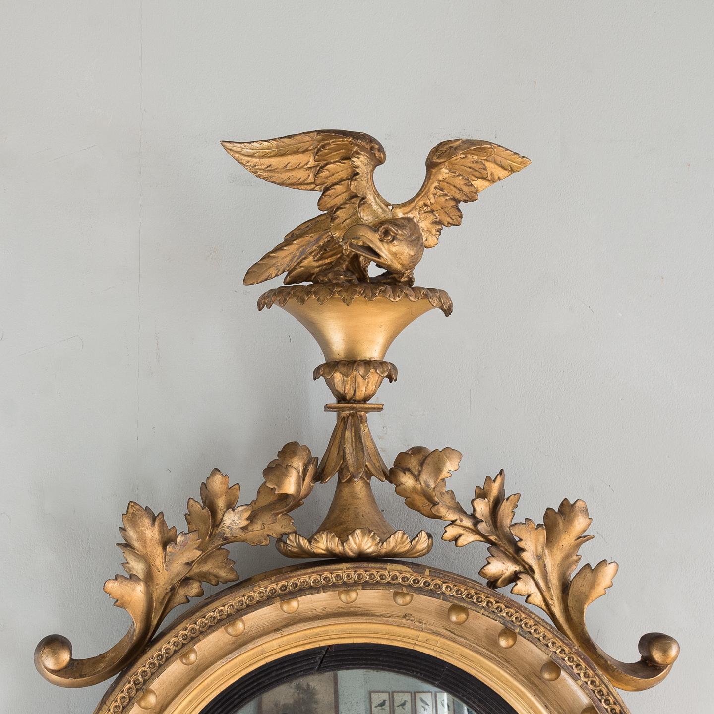 Regency giltwood convex mirror, English, circa 1825, having a well carved eagle on a rocky outcrop above interlocking leaf and scrolls leading to detailed circular frame including giltwood ball decoration, reeded ebonized slip and foxed mirror
