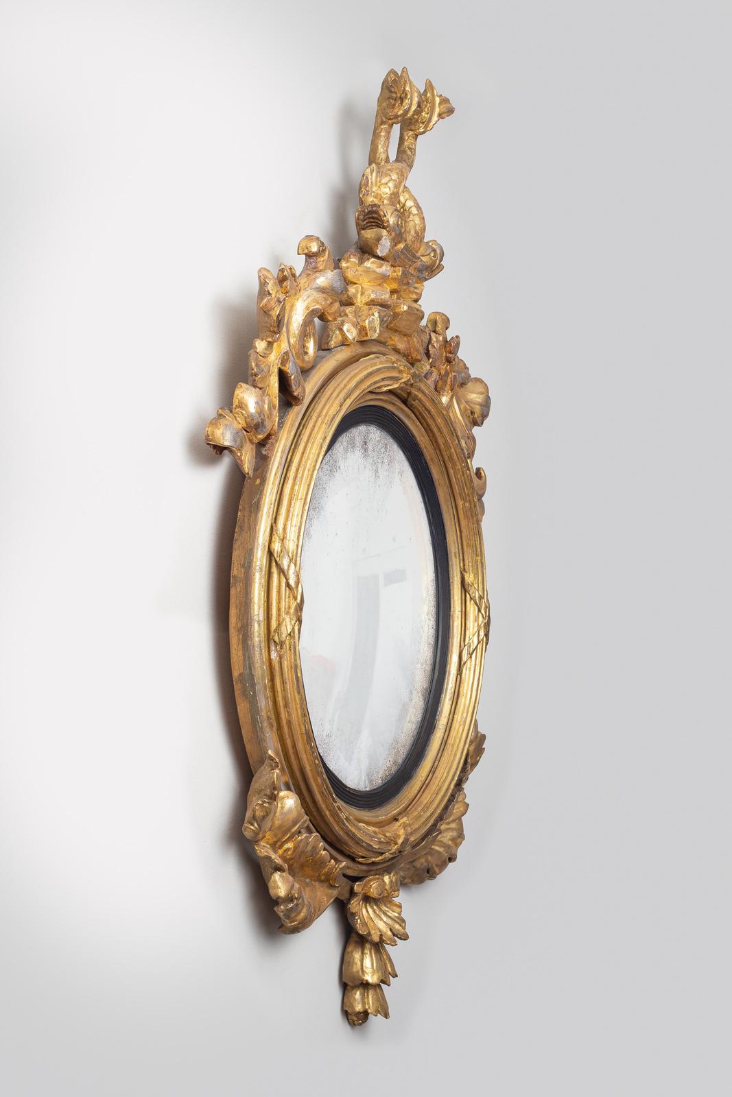 Period Regency giltwood convex mirror with crest of intertwined dolphins, sides decorated with carved acanthus leaves and carved shell undermount. Some wear to the gilding.