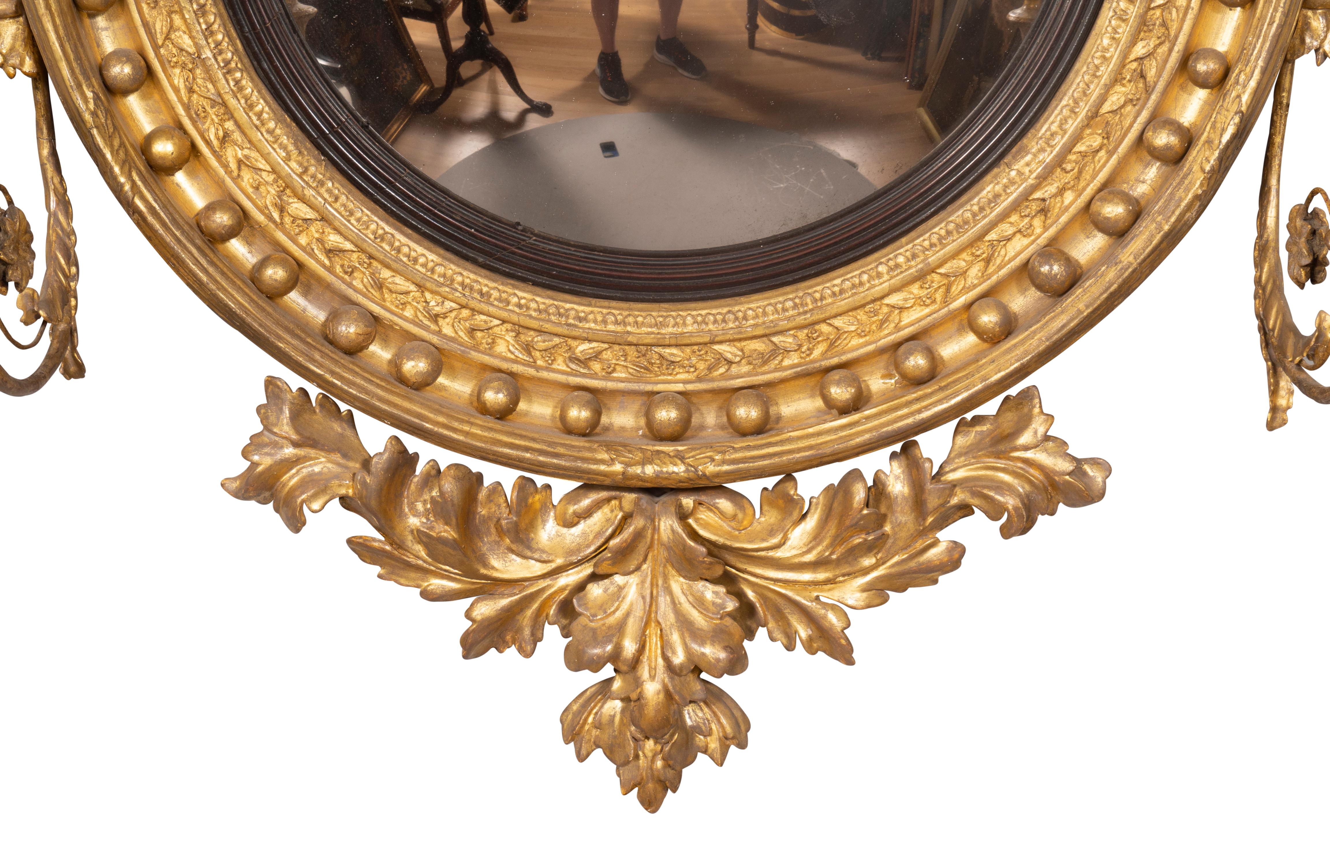With carved eagle holding two balls on a chain over a convex glass mirror with ebonized outer band, the conforming frame with spherules, mounted candle arms and base leaf carved decoration. Original gilding in great condition.
