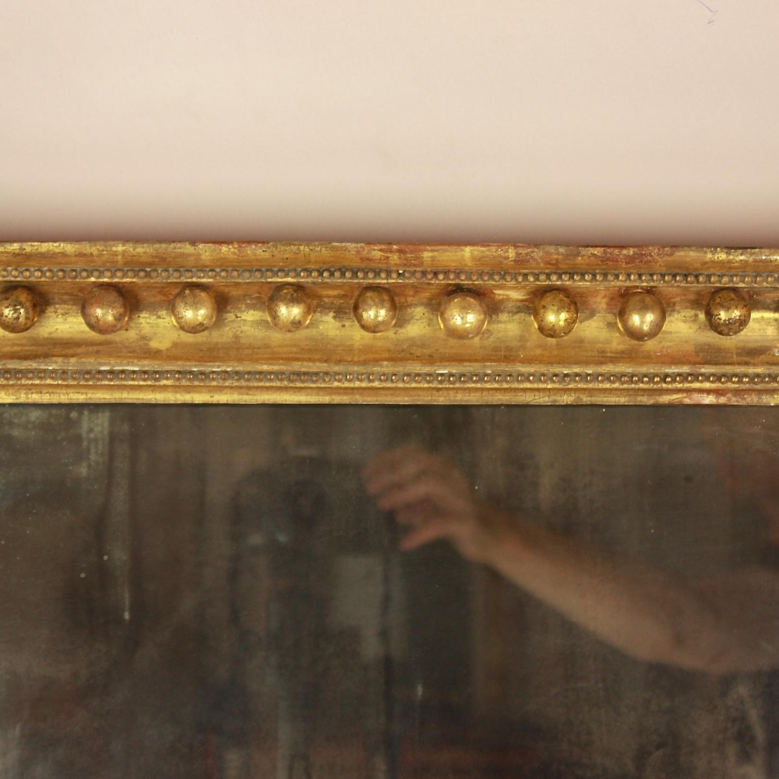 An early 19th century Regency giltwood mirror either of English or of American Federal origin. The original rectangular mirror plate set within a very fine water-gilded frame displaying an architectural cornice decorated with spherule-shaped