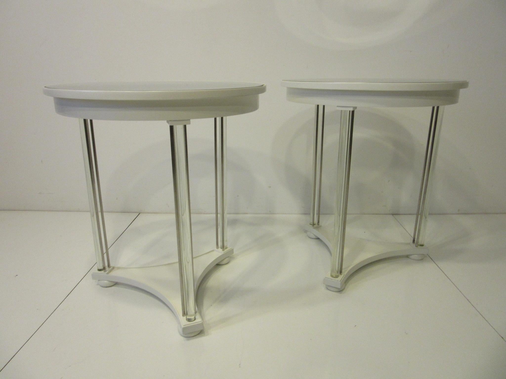 A pair of egg white wood side tables with glass and silver toned metal rod legs having a inset round glass and mirrored top sitting on wood bun styled feet. A sharp simple looking pair of tables that glistens in the light refracting off the heavy