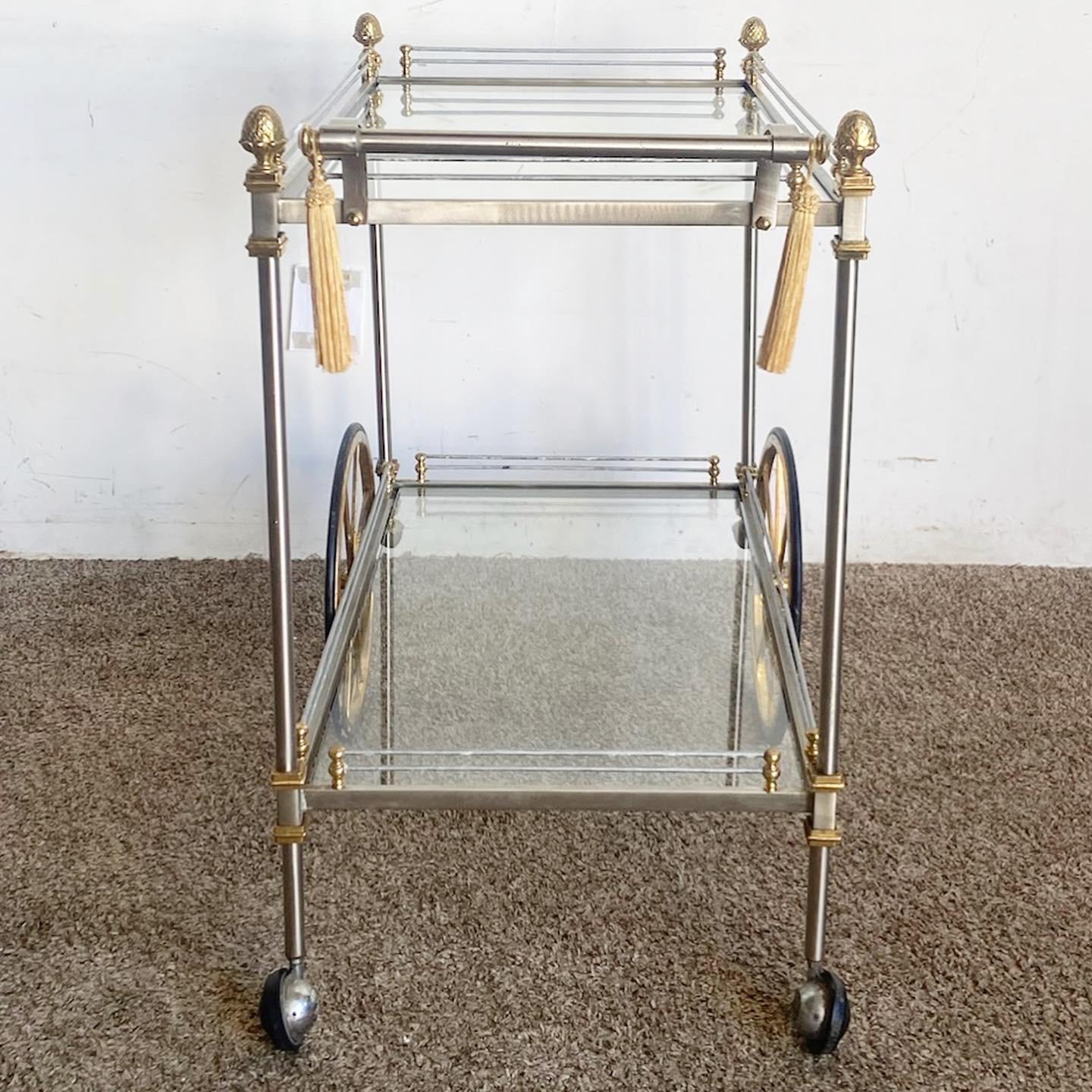 Experience the epitome of luxury with the Regency Metallic Two-Tier Bar Cart. Adorned in gold and silver finishes, its opulent frame is complemented by clear glass shelves, blending classic Regency charm with modern sophistication. Beyond its