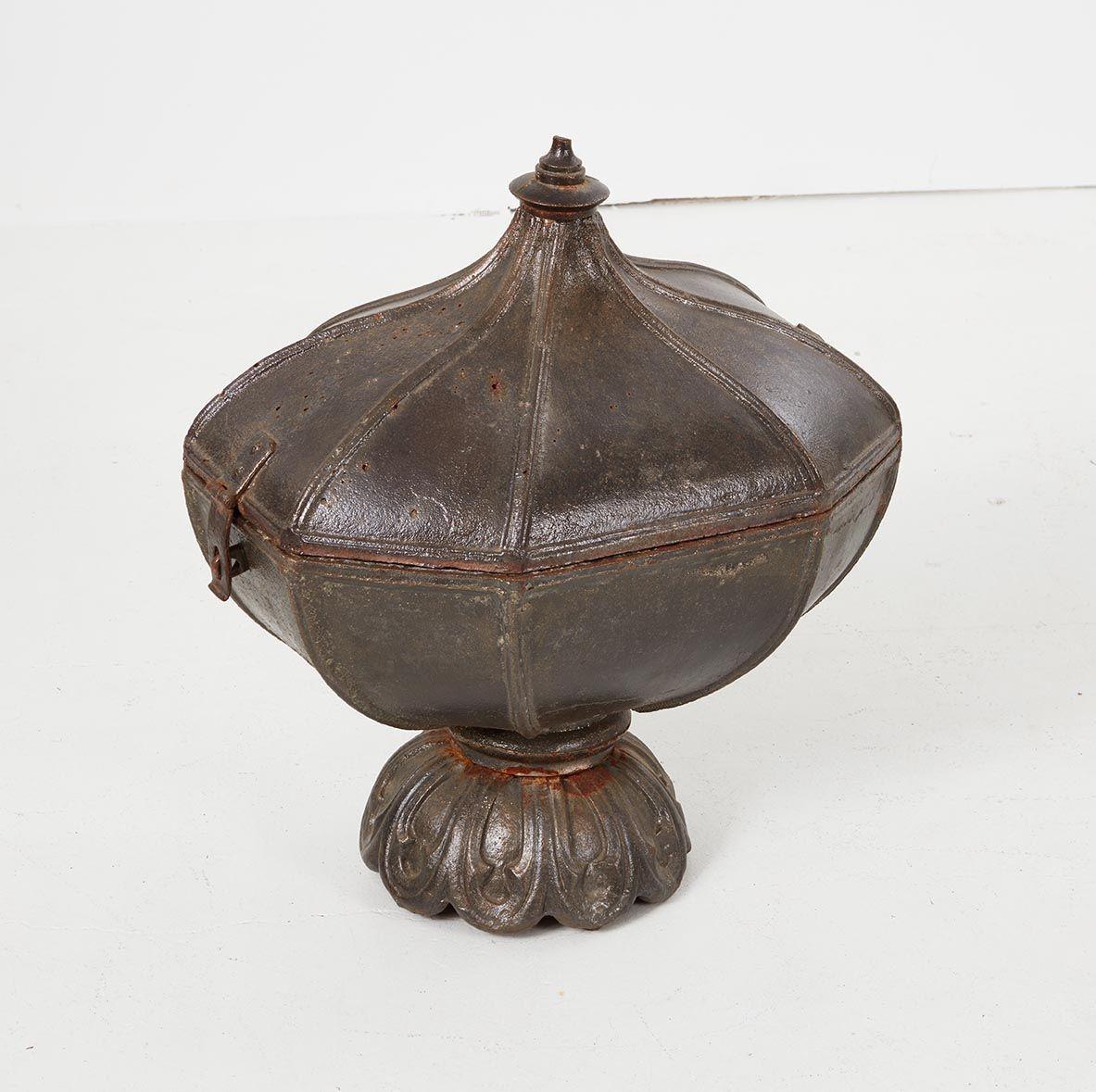 A shaped Regency period room warmer in the form of an elongated allium bulb with curved sides and octagonal ribs, with integral lid and decorated footed base, constructed of heavy cast iron. Sinuous shape and attractive polished ash-grey surface.