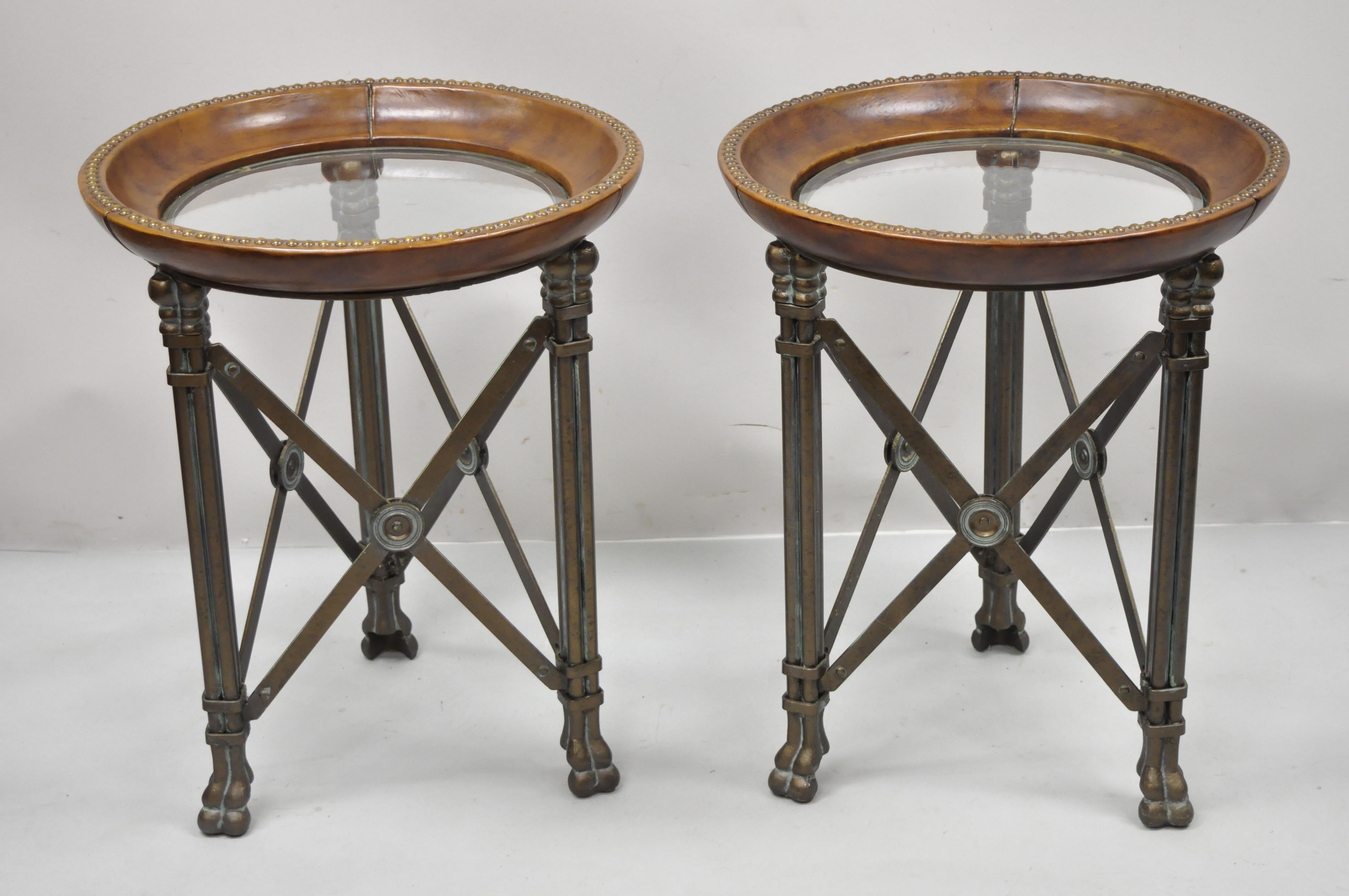 Regency iron brown leather round glass top end tables attributed to Maitland Smith - a Pair. Item features metal stretcher base with paw feet, brown leather rim, round glass top, heavy metal frame, American craftsmanship, great style and form. Circa