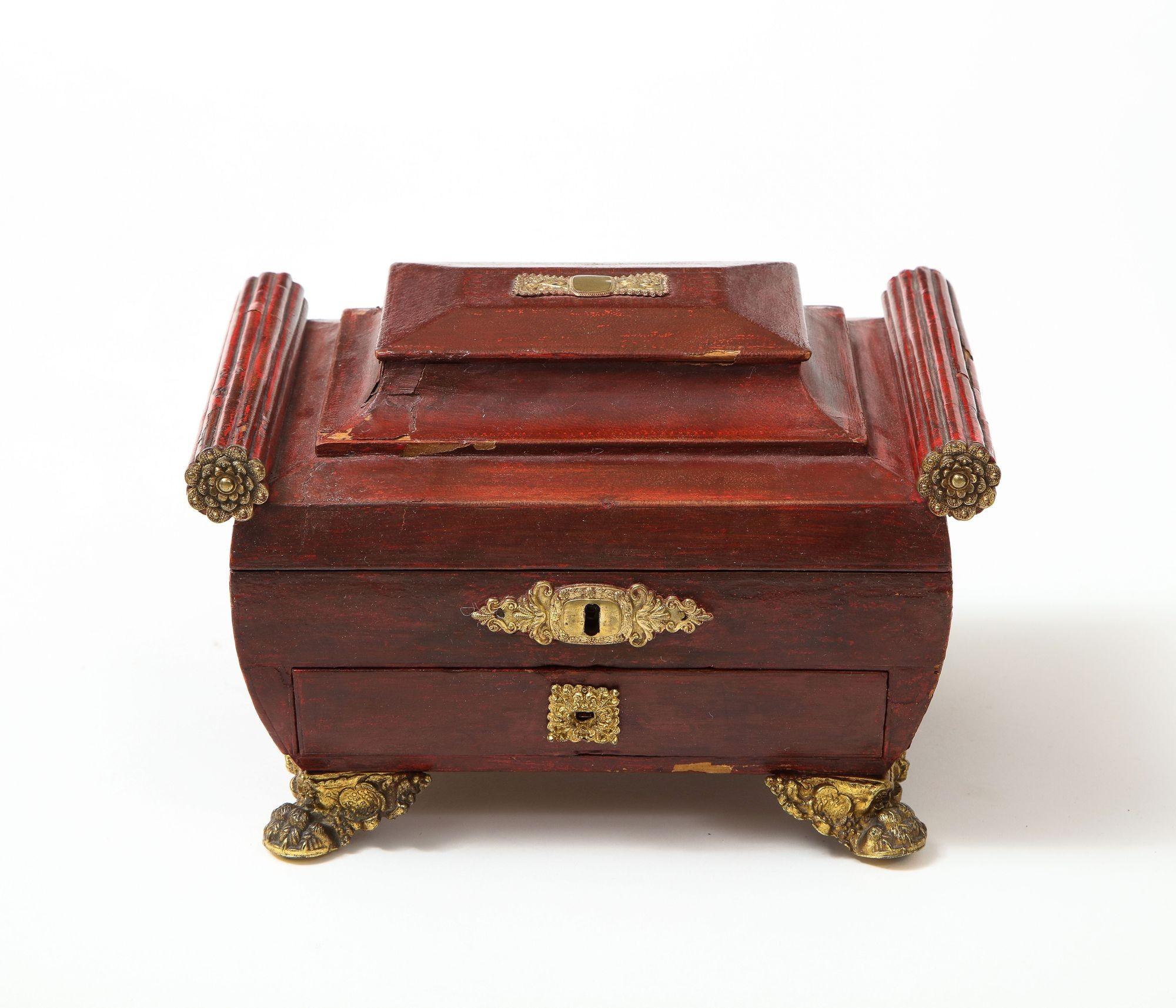 Regency leather covered sarcophagus shaped sewing box with gilt repoussé brass mounts and ribbed bolster ends over heavily molded top, the bombe body standing on flower adorned paw feet, the interior with fitted compartments and leather pouches, the