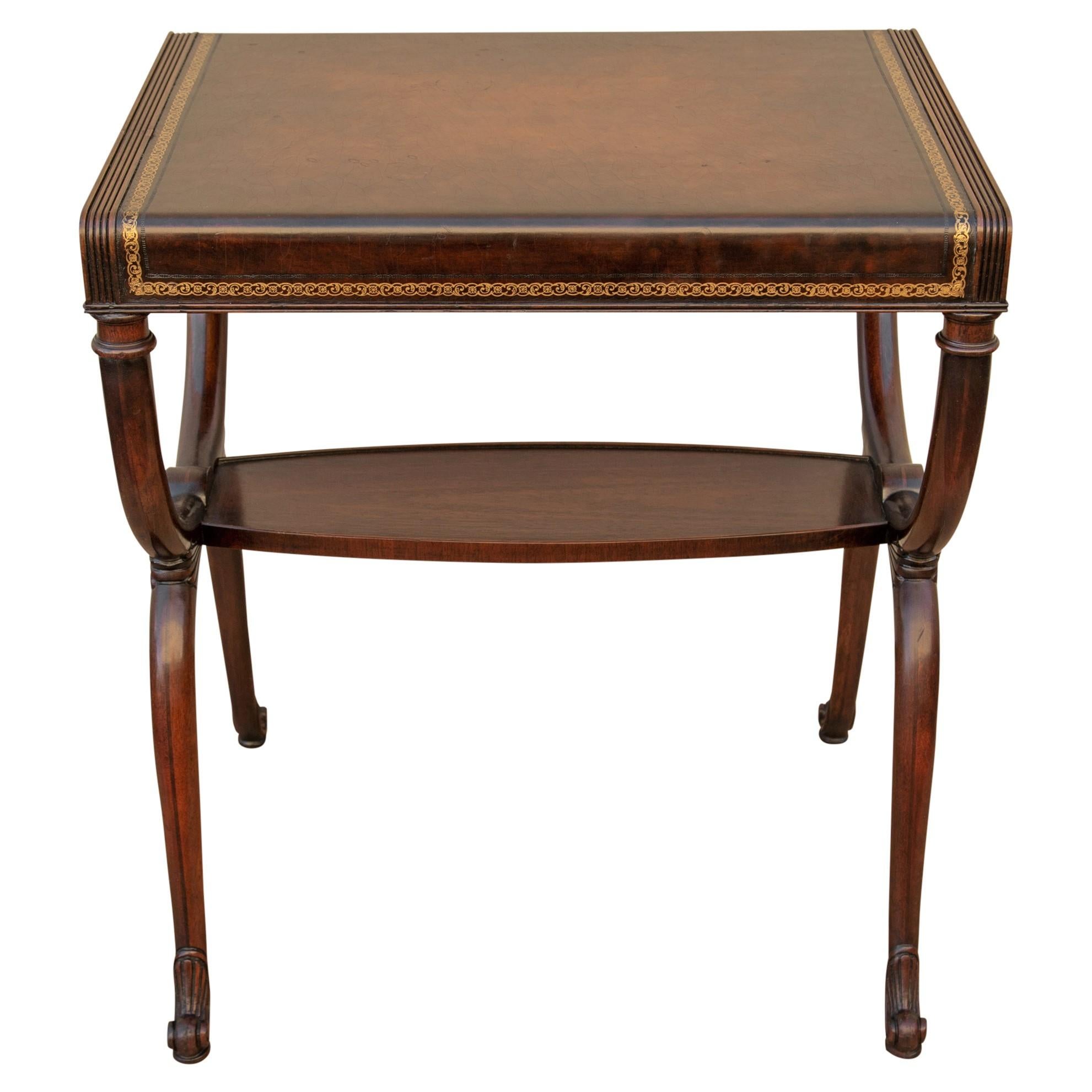 Regency style mahogany and leather foyer or end table with Curule legs by Weiman, circa 1950s. It has a tooled and gilded leather top, curved legs with brass ring lion head hardware, reeded sides above flame mahogany aprons and carved escargot feet.