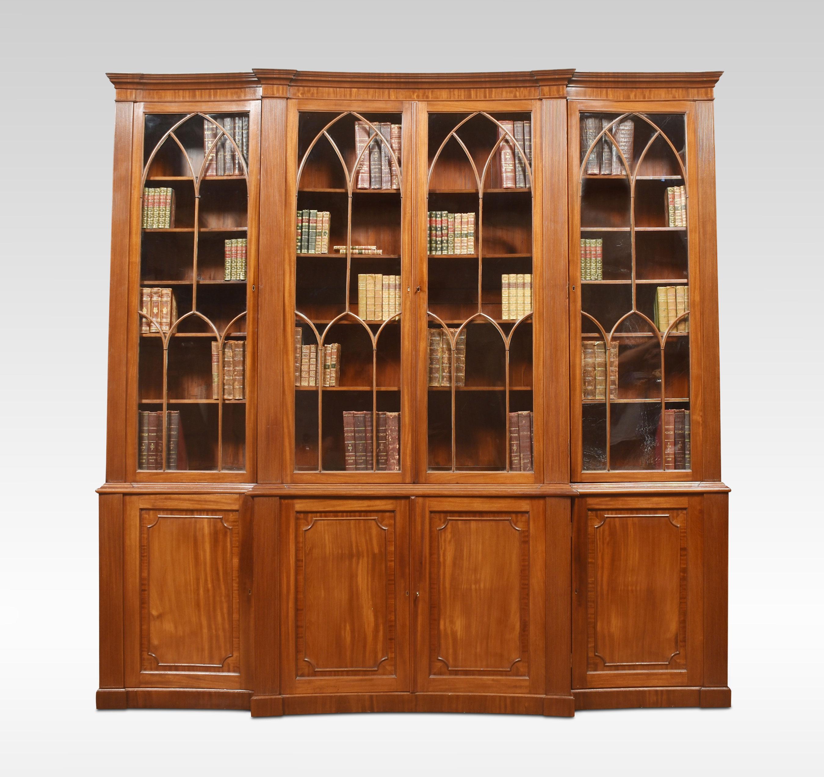 Mahogany breakfront library bookcase, the concaved moulded cornice, above four large curved astragal glazed doors opening to reveal adjustable shelved interior flanked by reeded columns. The base section is fitted with central panelled doors opening