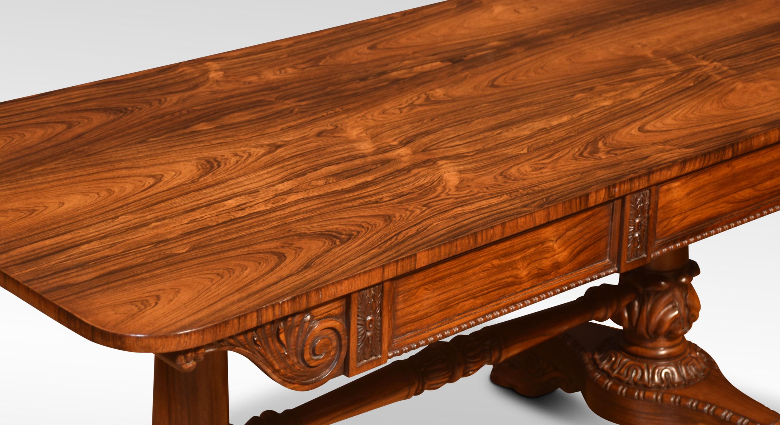 Rosewood library table, the rectangular top with rounded corners, above two frieze drawers, raised on tapering columns and acanthus carved socles, raised on egg and dart moulded trestle ends, terminating in lions paw feet and concealed