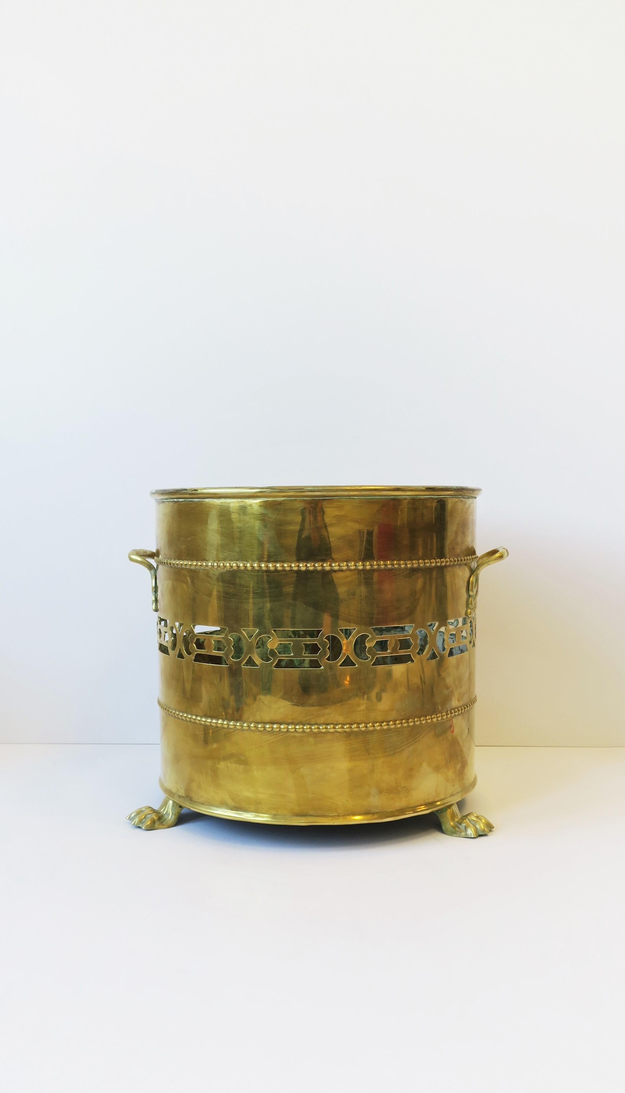 A substantial brass cachepot jardinière plant pot holder with lion design in the Regency style, circa 20th century, England. Piece is brass with a tri-lion paw feet base, handles on either side, and bead and perforated design around. Dimensions: