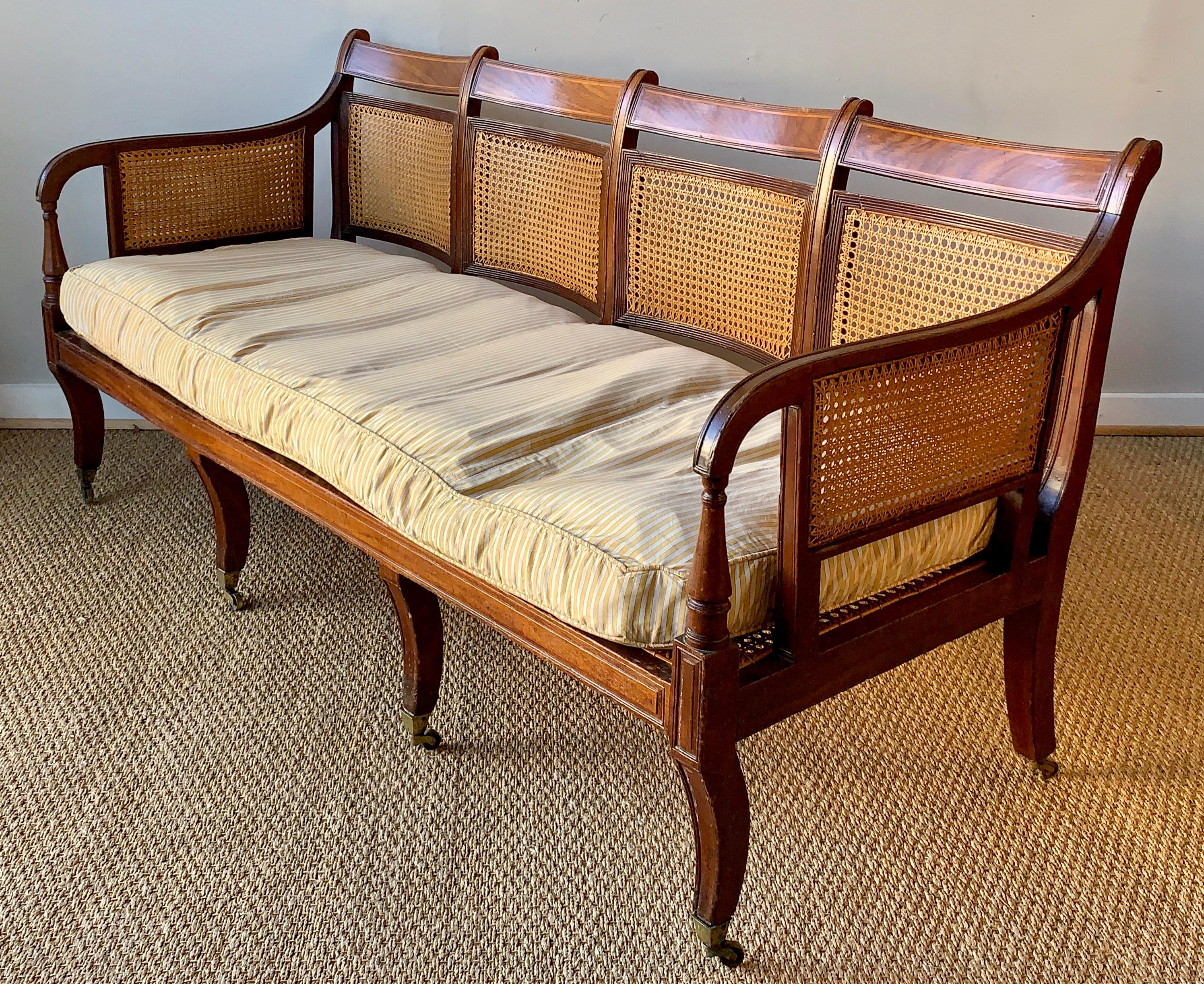 An early 19th century English mahogany and satinwood settee with cane back, seat and arms with custom down filled cushion.