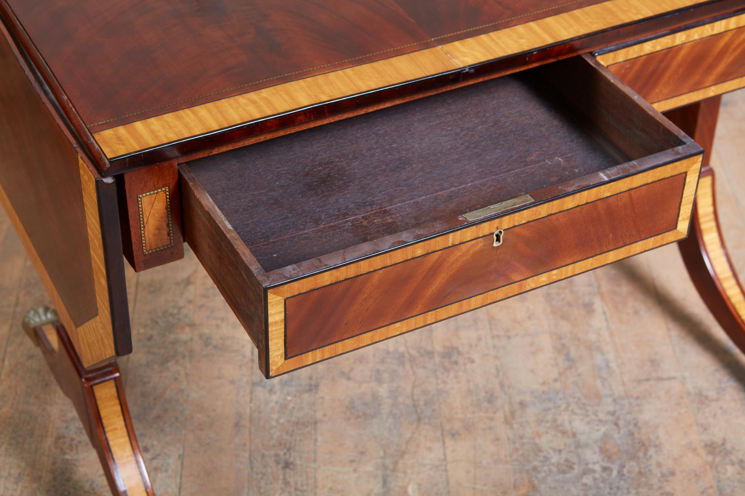 Regency period flame mahogany and satinwood banded sofa table, the vividly grained top with canted corners, the satinwood banding with ebony string borders, the two drawers similarly treated and retaining original locks, standing on downswept legs