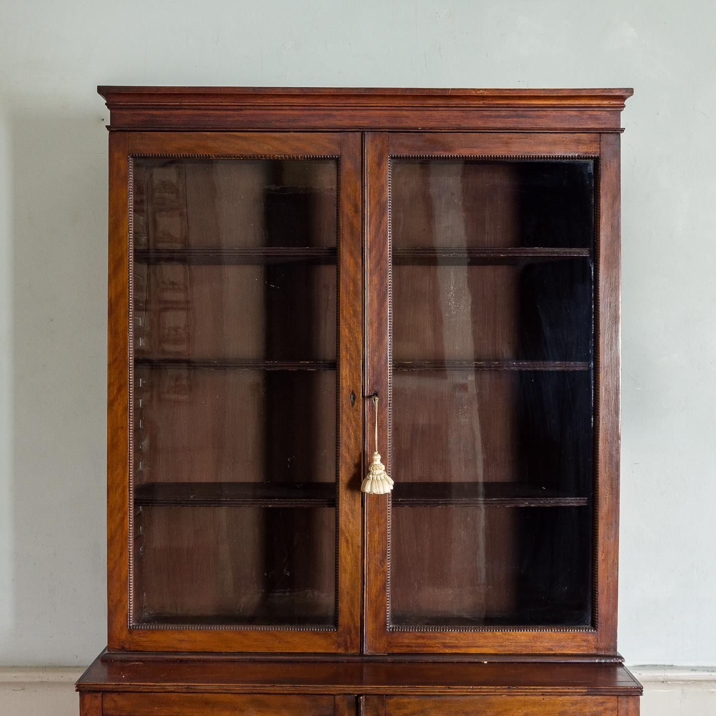 Regency mahogany bookcase, English, circa 1825, having a moulded cornice with plain frieze above glazed doors enclosing three adjustable shelves, leading to reeded section above two glazed doors with pleated green fabric within. Raised on bracket