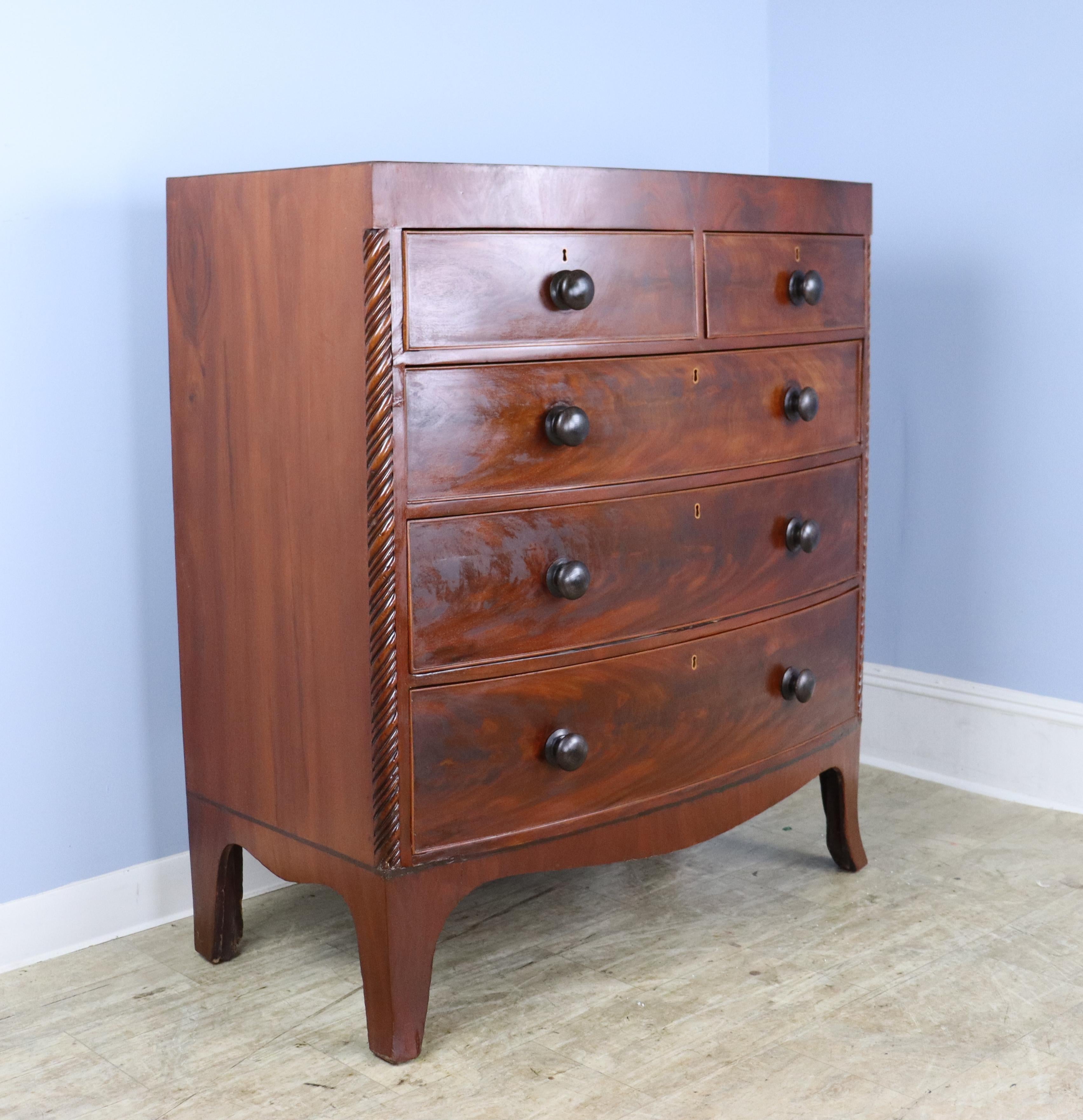 A handsome early bowfront chest of drawers with spiral carved corner columns. The glowing mahogany veneer is in good antique condition, as is the cockbeading around the drawers. Inside the 5 roomy drawers are traces of the original blue paper. Nice