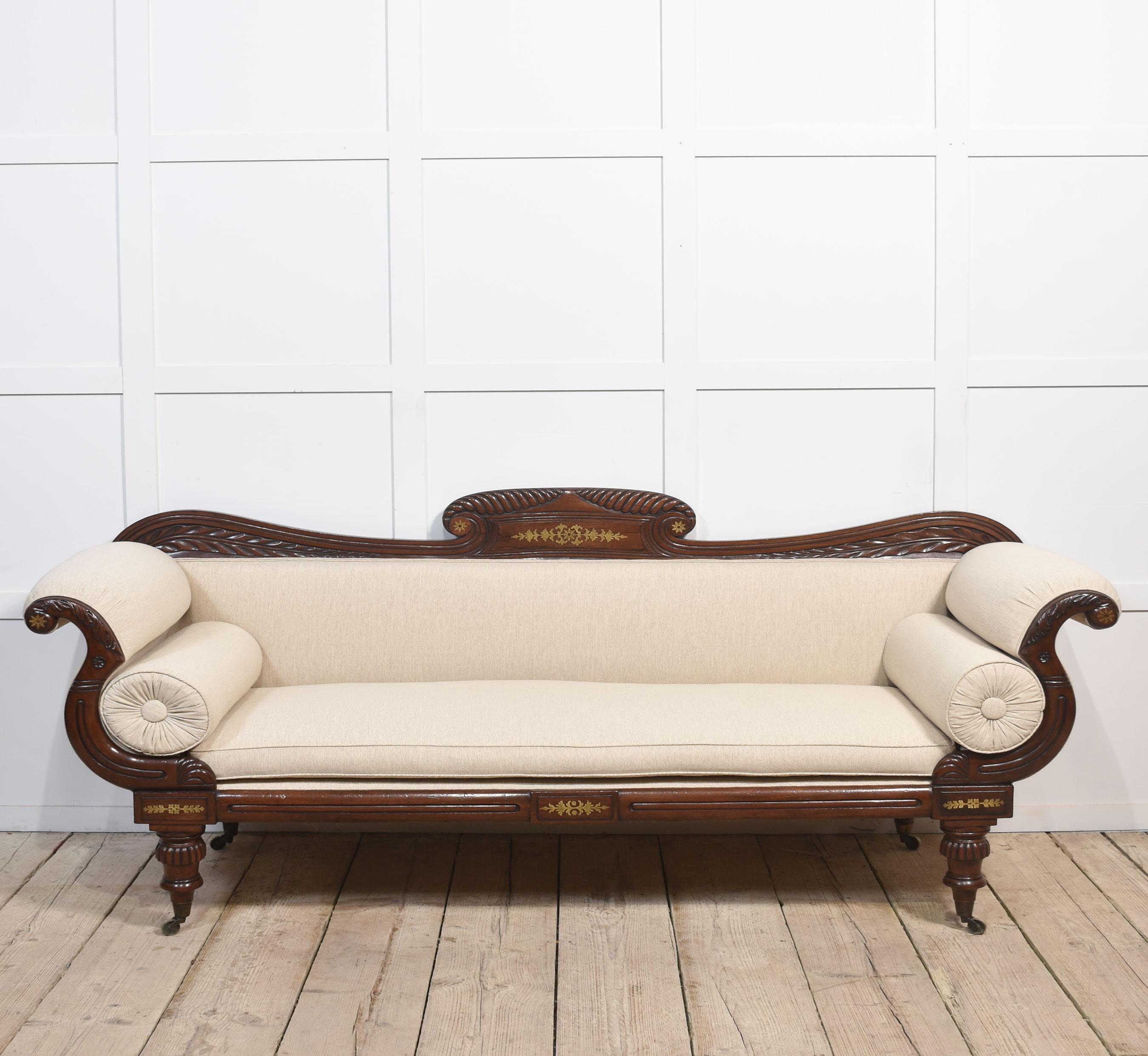 Early 19th-century mahogany framed scroll end settee, the acanthus scrolling arched top rail with brass detail above back and seat flanked by scrolling upholstered arms. Standing on foliated tapered legs with brass caps and