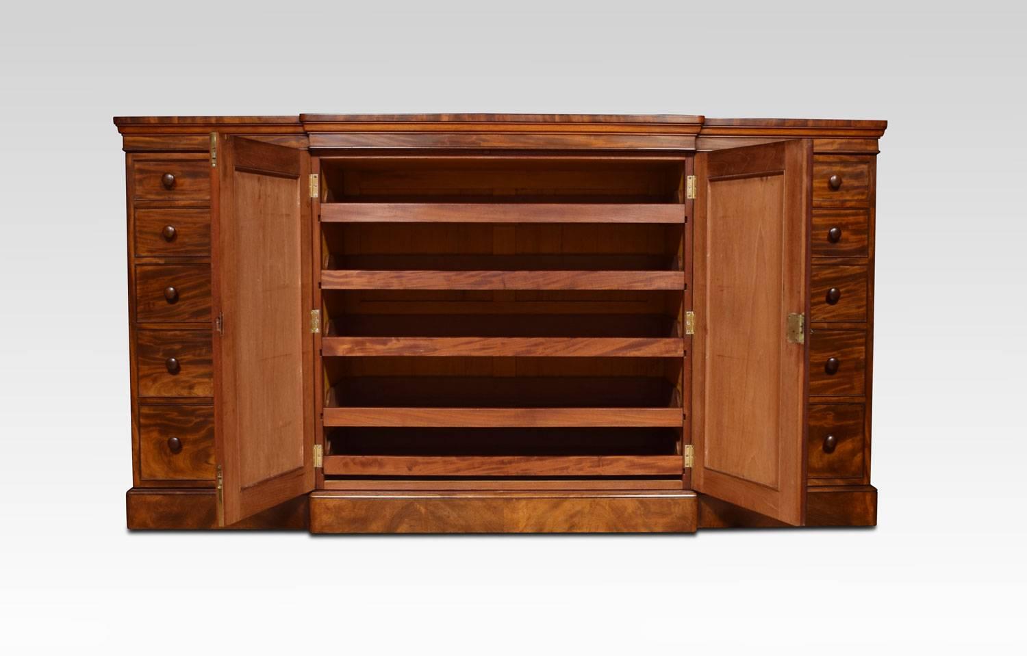 Regency mahogany, dwarf press cupboard, the large rectangular moulded top above two flame mahogany panelled centre doors. Enclosing five sliding trays. Flanked by a bank of five drawers on either side with turned handles. All raised up on plinth