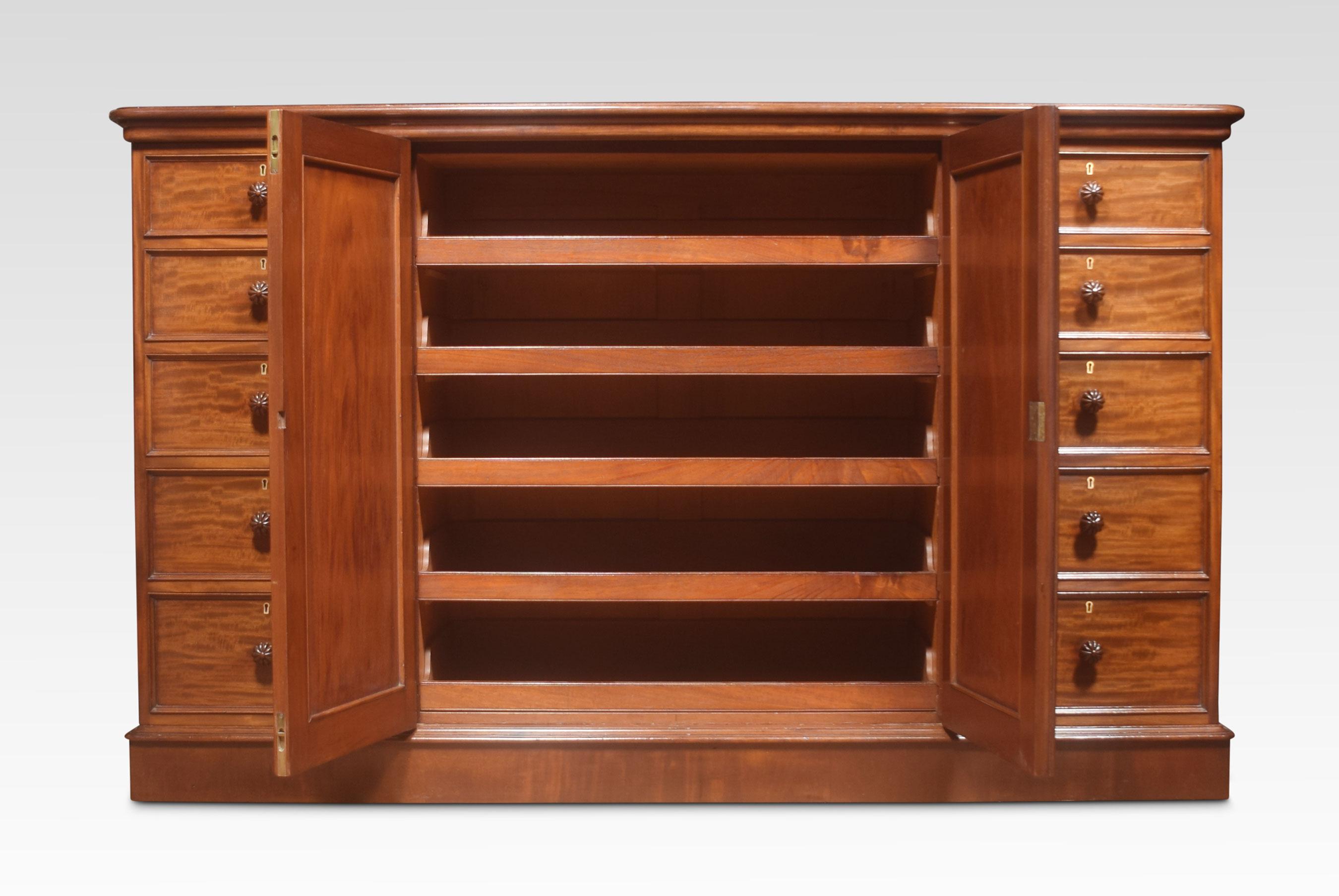 Regency mahogany, dwarf press cupboard, the large rectangular moulded top above two flame mahogany panelled centre doors. Enclosing four sliding trays. Flanked by a bank of five drawers on either side with turned handles. All raised up on plinth