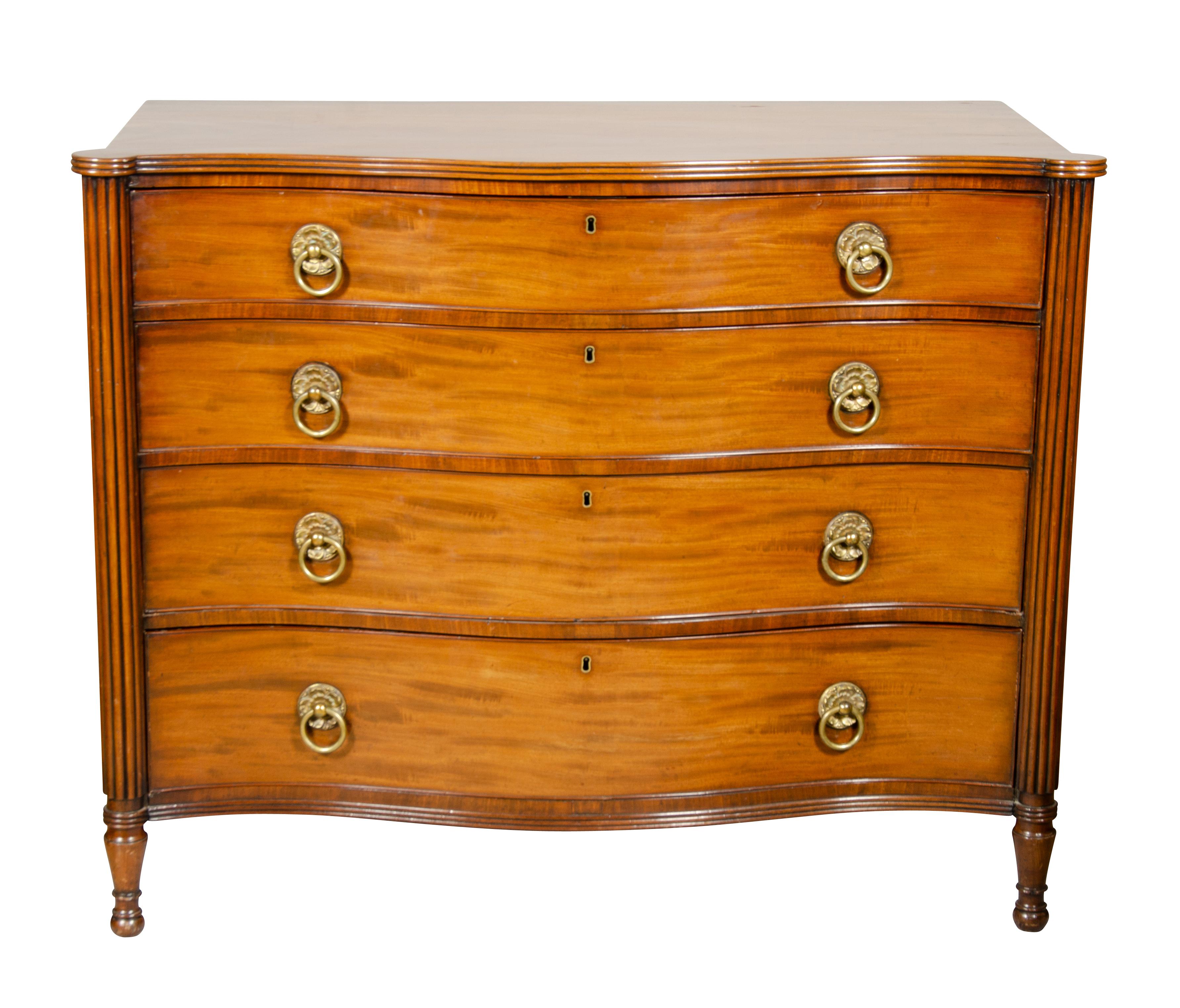 Serpentine top over four graduated drawers flanked by reeded columns. Brass ring handles on drawers , raised on circular turned tapered legs.