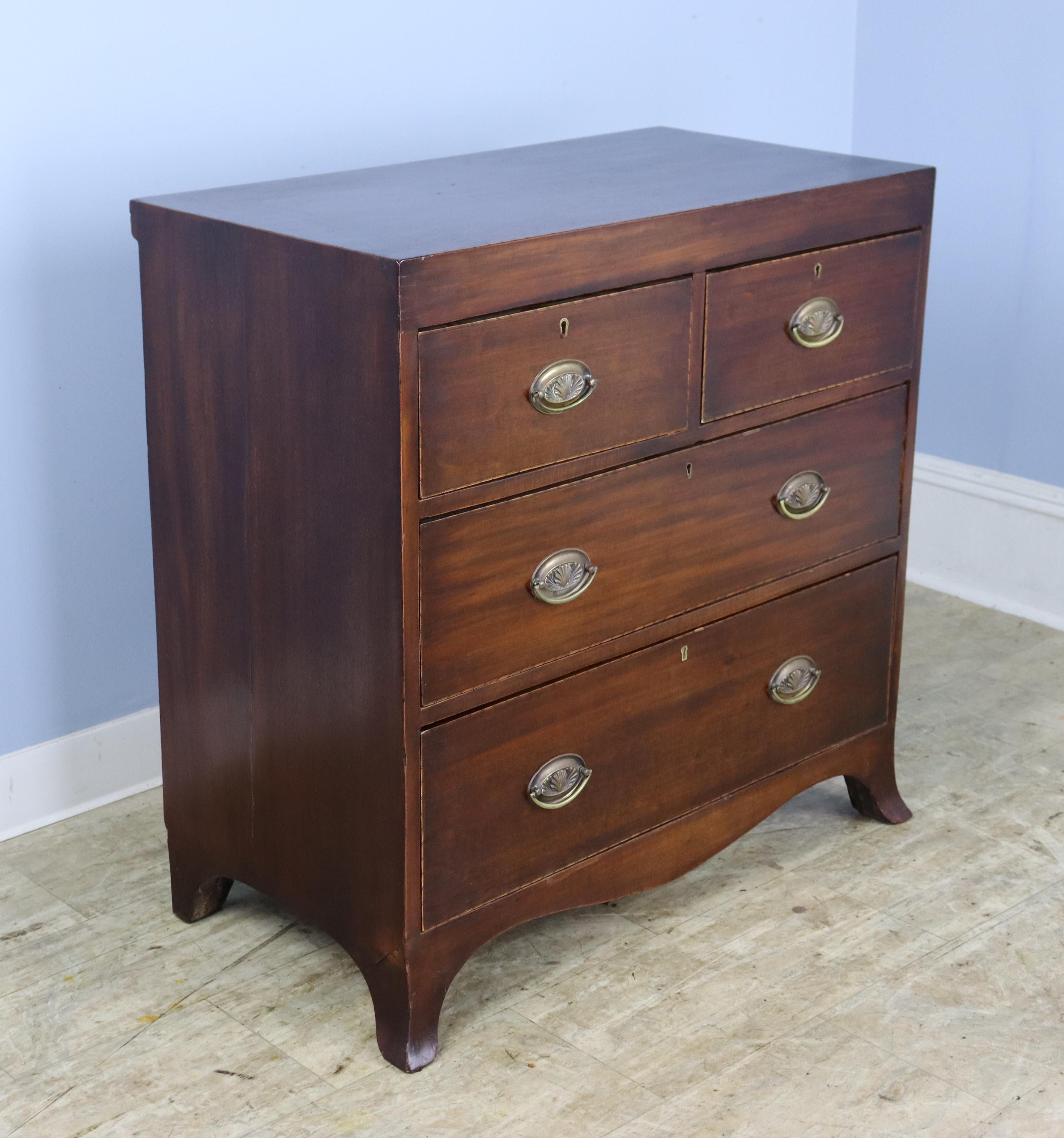A small chest of drawers from the Regency period with flared feet and delicate intricate stringing around the top and drawers, in good antique condition.  Classic two over two construction.  Original oval braases.  There is some wear on the feet