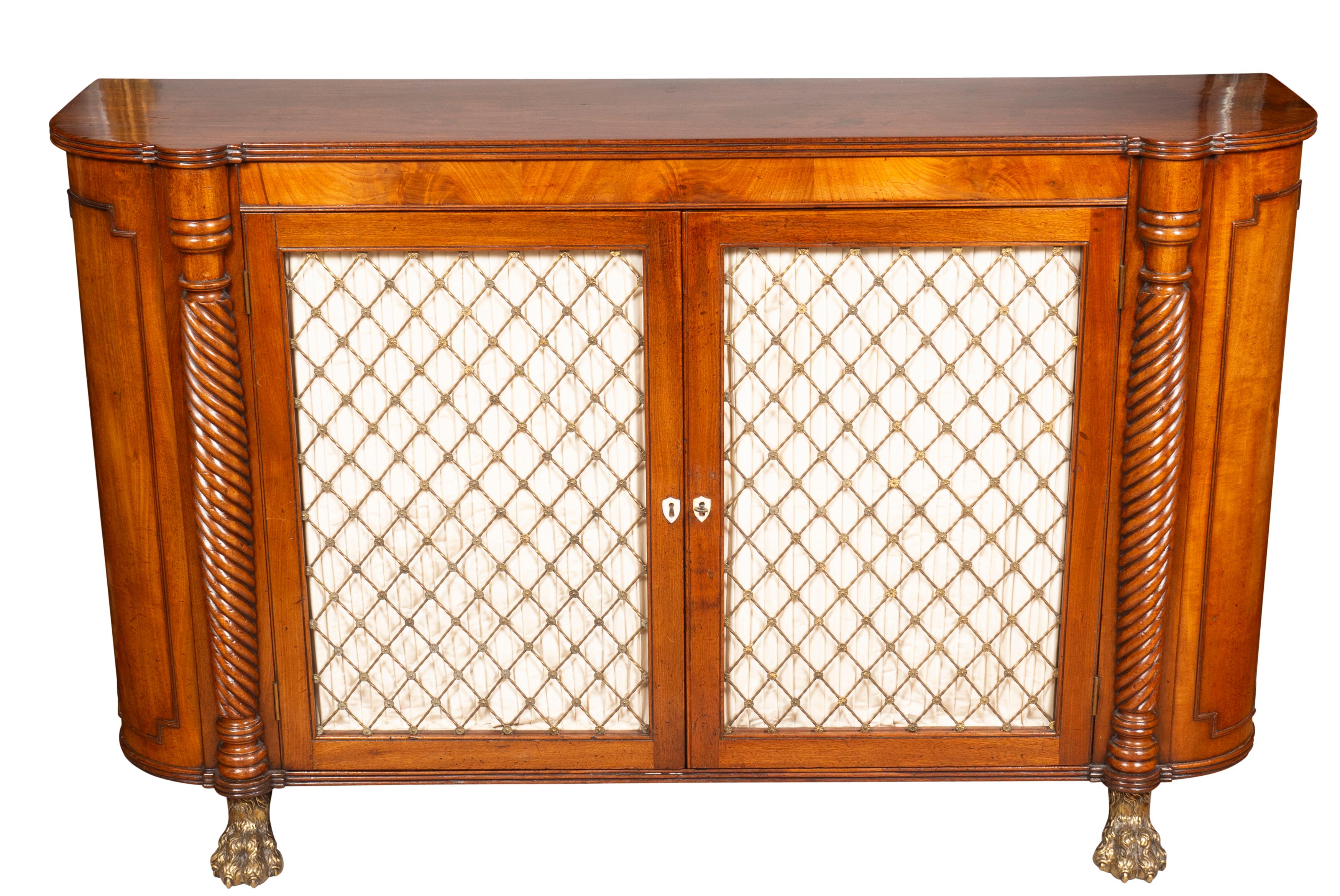 Classic form with rectangular top with rounded ends over a pair of brass grill doors flanked by spiral reeded columns and raised on brass lions paw feet. One shelf and key.