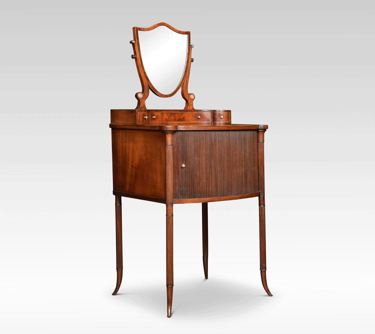 Regency mahogany dressing table the raised shield shaped mirror supported on slender supports having an arrangement of short draws below. The shaped moulded top above unusual tambour front cupboard. All raised up on reeded legs terminating in
