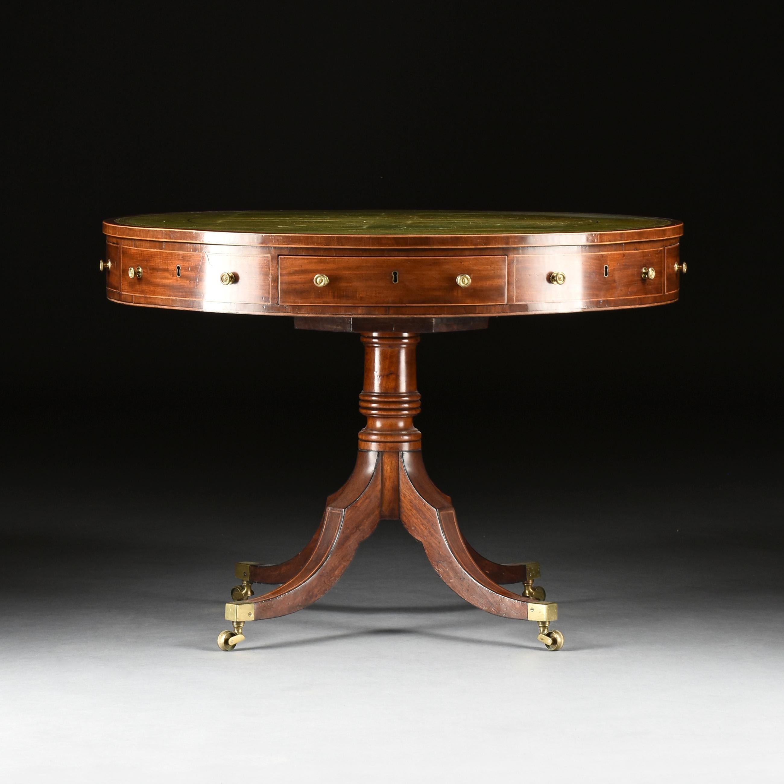 Circular top with green tooled leather and crossbanded edge. Turned support joined by four square section saber legs ending on plain brass cup casters.