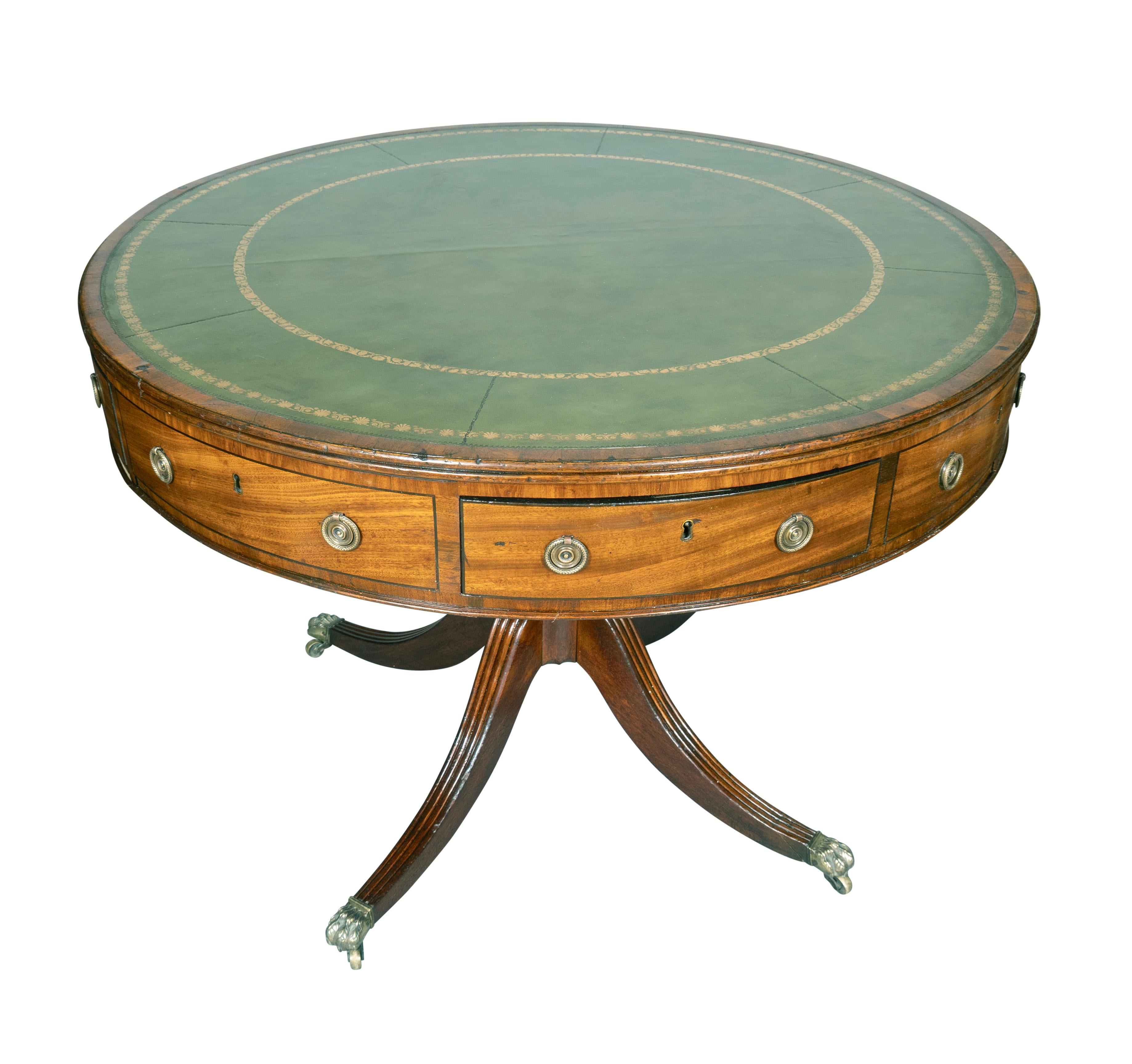 Insertion circulaire de cuir vert estampé sur le dessus et sur la tranche. Frise contenant des tiroirs alternés avec des poignées rondes en laiton et des plaques arrière. Support tourné avec quatre pieds sabres avec roulettes à pattes.