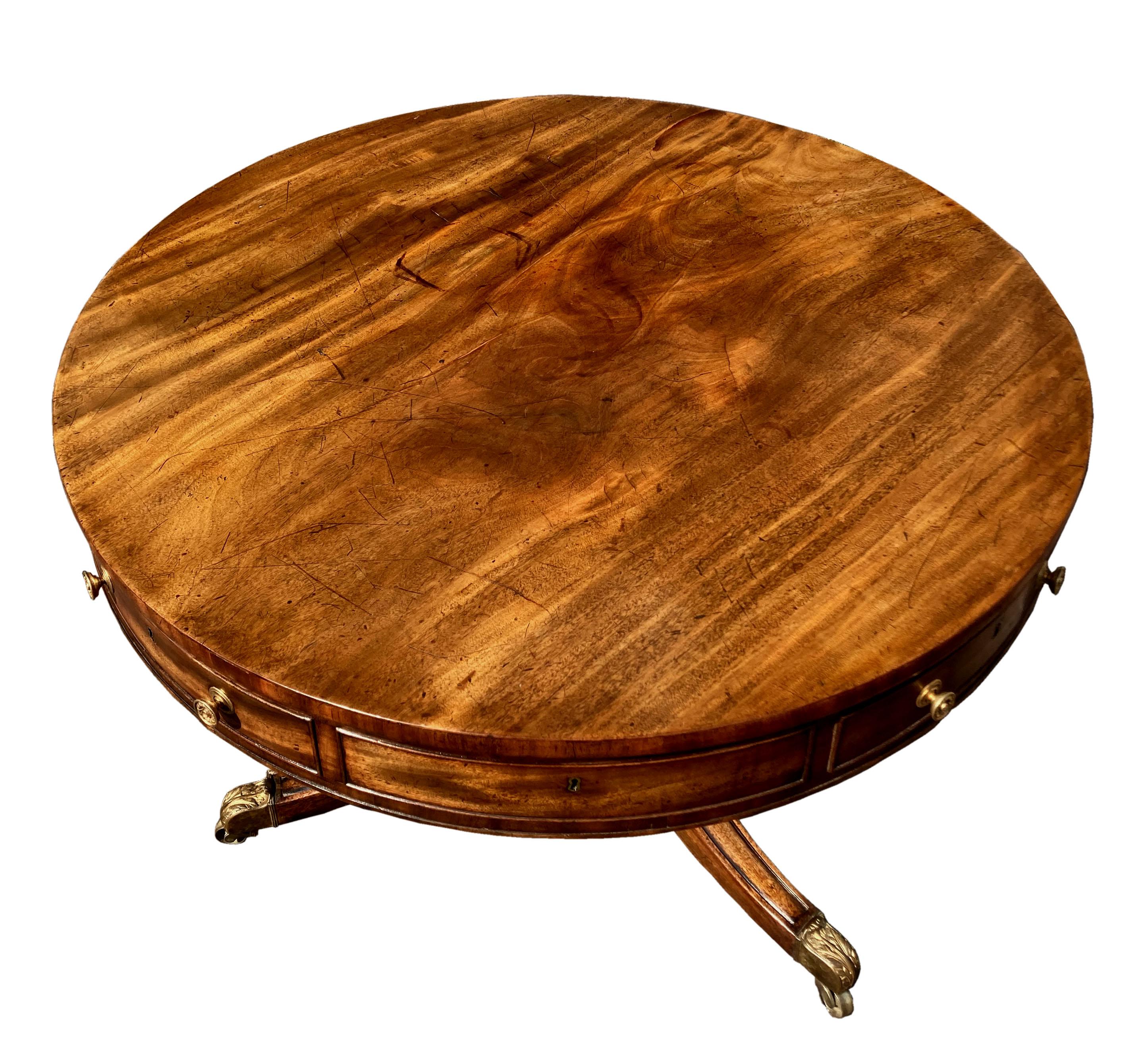 A Regency mahogany drum table of a good original colour and condition. Attractive model with veneered top, cross-banding to the edge of the top and carcase fronts and 3 splay sabre leg base with castors finely cast with acanthus leaves and still