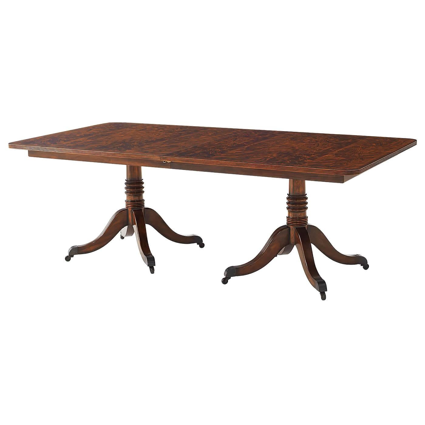 A mahogany veneer and solid twin pedestal extending dining table, the crossbanded reeded edge top with rounded corners opening to accommodate a matching leaf, above a banded frieze on two gun barrel turned columns each terminating in four downswept