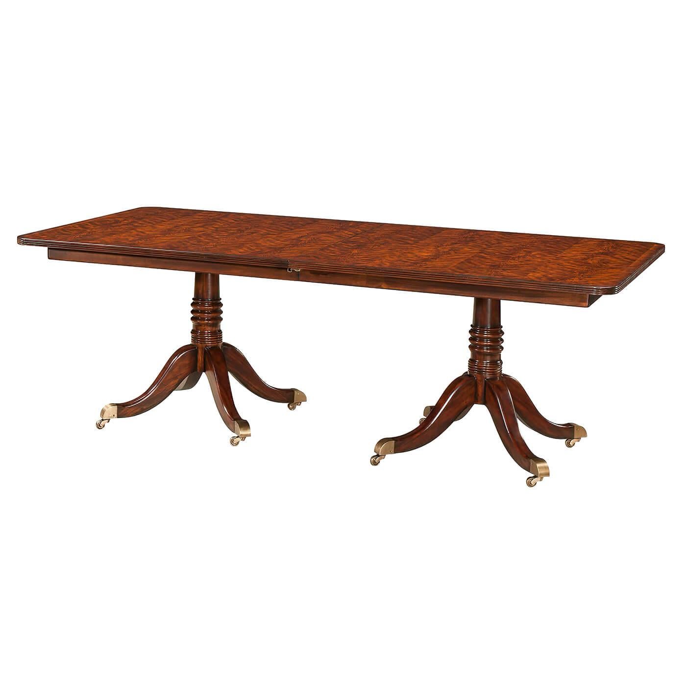 A mahogany veneer and solid twin pedestal extending dining table, the crossbanded reeded edge top with rounded corners opening to accommodate a matching leaf, above a banded frieze on two gun barrel turned columns each terminating in four downswept