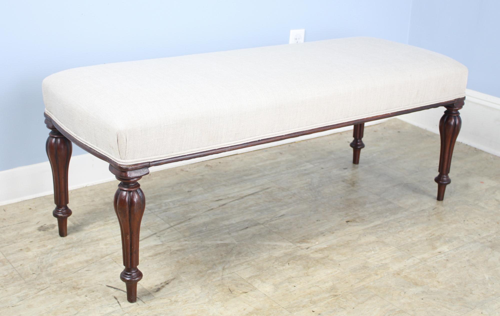 An elegant stool newly covered in French beige linen, with decorative piping at the edge of the seat. Graceful and well-shaped ends. Constructed with mahogany legs, circa 1830 that are well-carved and sturdy. Very good sitting-height, comfortable
