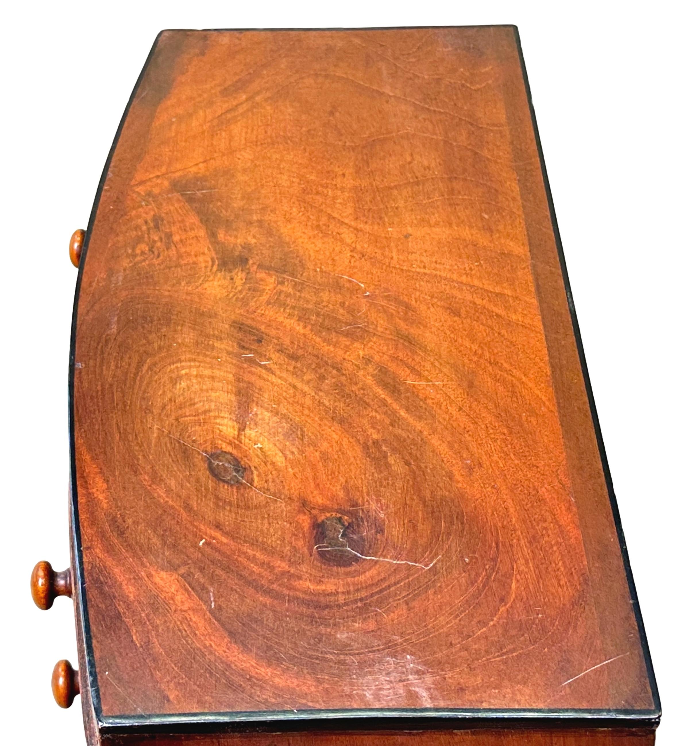 Una cassapanca in miniatura in mogano di tarda Reggenza di ottima qualità, di forma arcuata, con il piano ben rifinito con cordoni ebanizzati, due cassetti corti e tre lunghi che conservano i pomelli originali in legno tornito, sopra un elegante