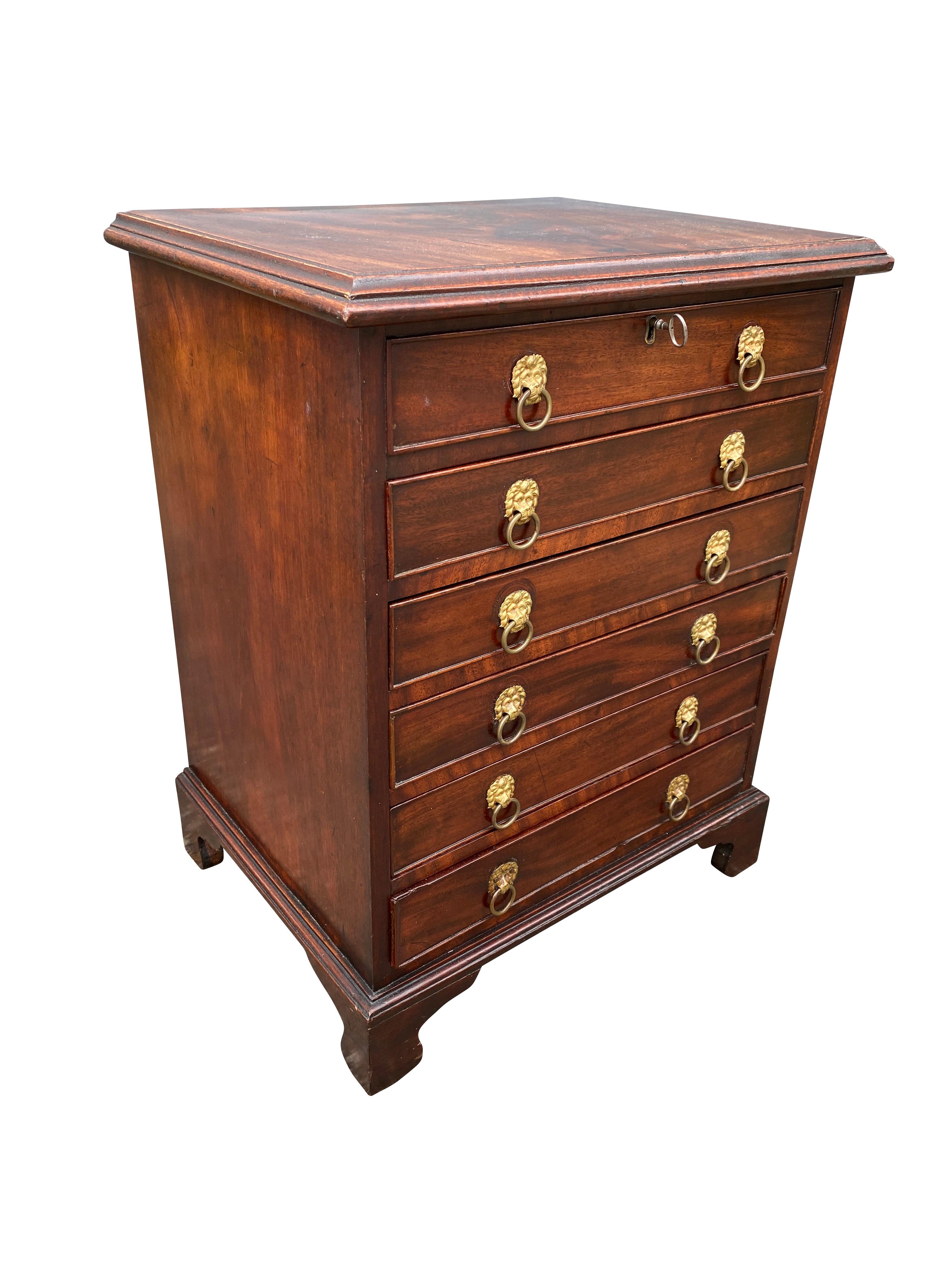 Rectangular hinged top enclosing a well over a false drawer over five working drawers, bracket feet. Loins head brass handles. Has key. Sold Moore & Co NYC., 1989.
