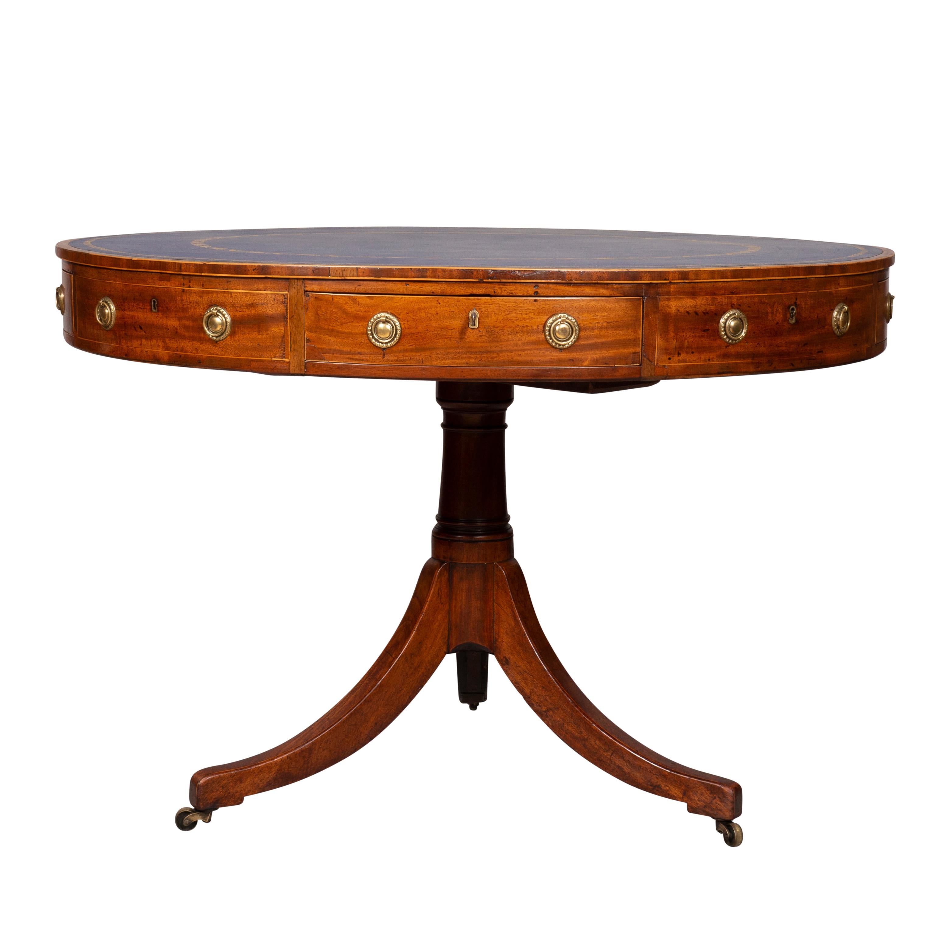 With an oval top with cross banding and blue tooled leather over a frieze with drawers with brass ring handles, raised on a columnar support and tripartite base with saber legs. Casters. Newport Rhode Island Estate.