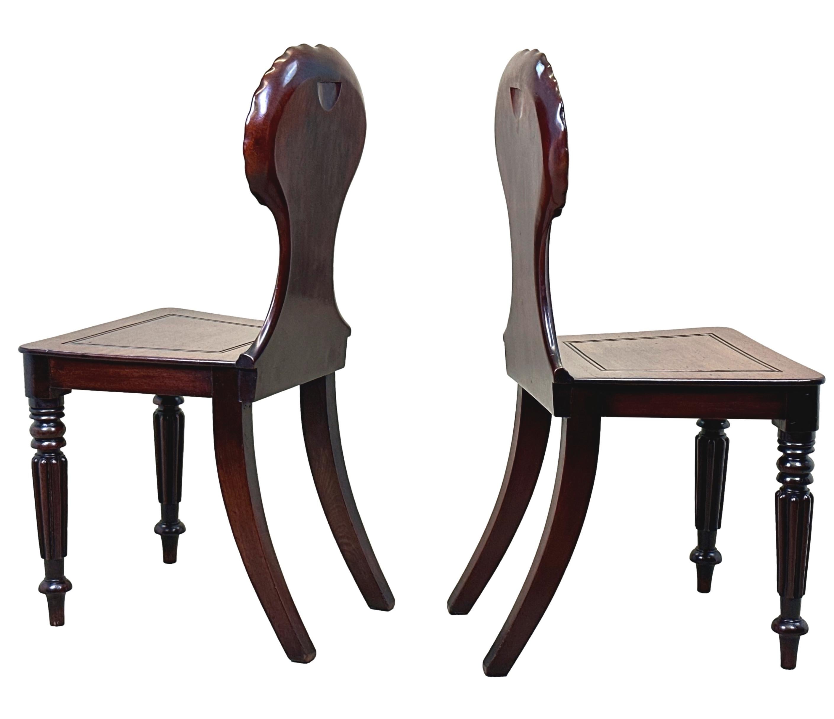 A Very Fine Quality Pair Of Early 19th Century, Regency Period, Mahogany Hall Chairs, In The Manner Of Gillows Of Lancaster, Having Deeply Carved Shells To Elaborate Backs, Over Panelled Seats Raised On Elegant Reeded Turned And Tapering Legs,